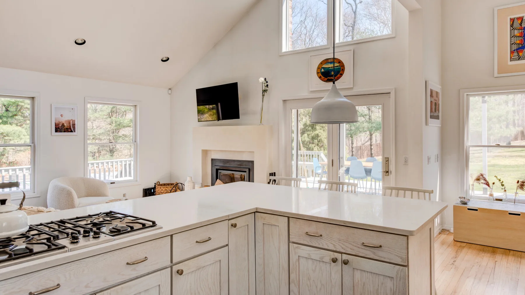 Una cocina luminosa se abre a un comedor con grandes ventanas y techo alto.