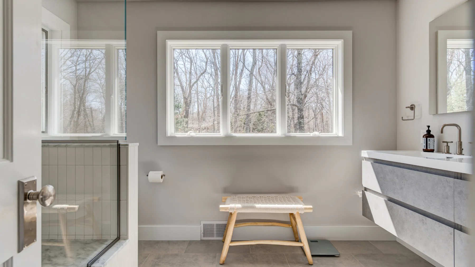 Un baño con ducha de vidrio, lavabo y banco bajo la ventana.