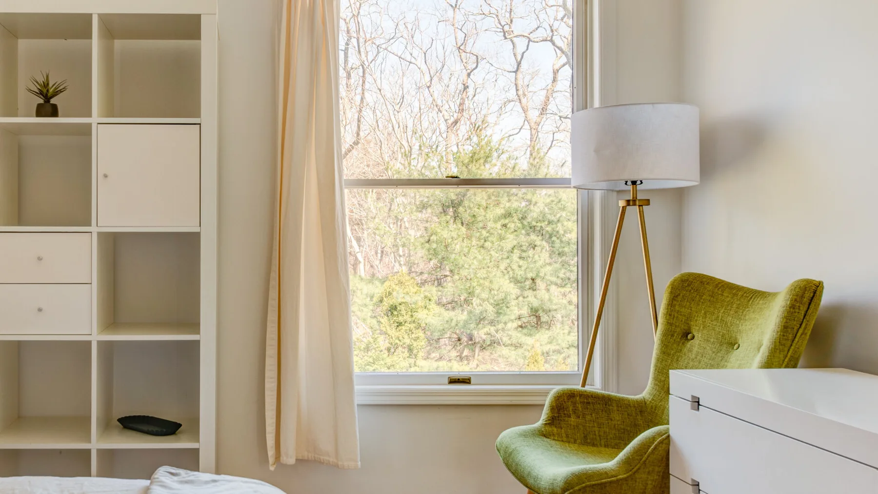 Una habitación luminosa con un sillón verde junto a una ventana grande.