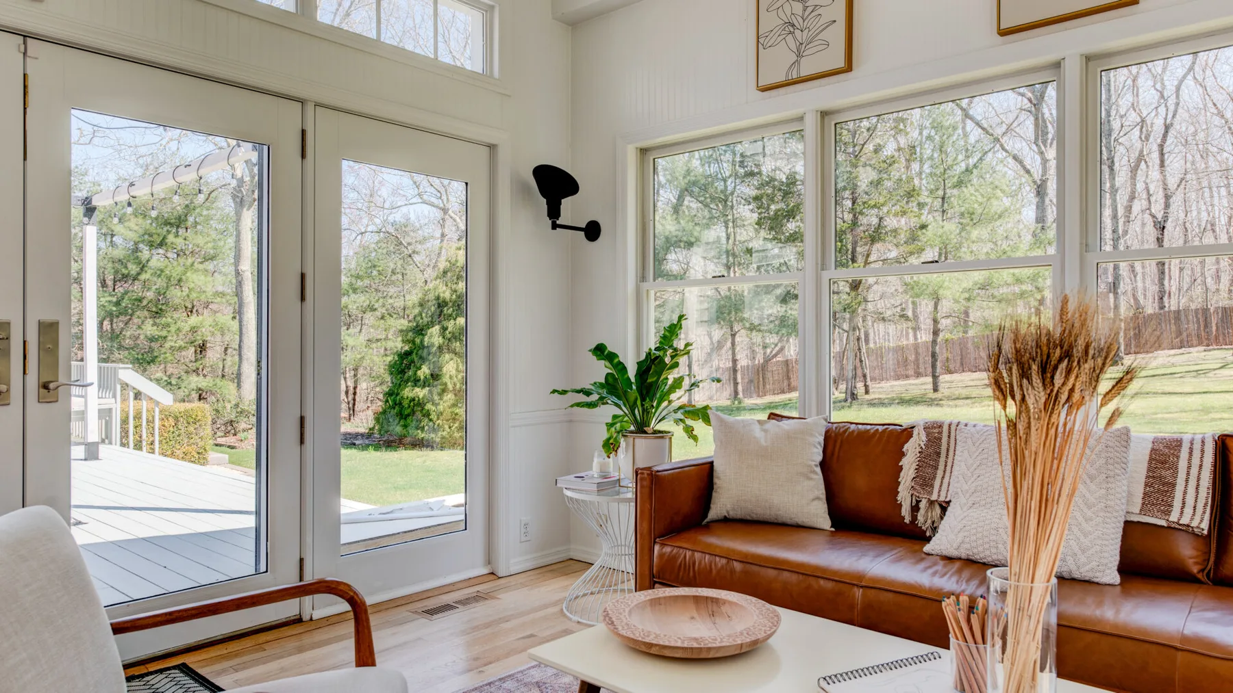 Una sala luminosa con un sofá de cuero junto a grandes ventanas con vista a los árboles.