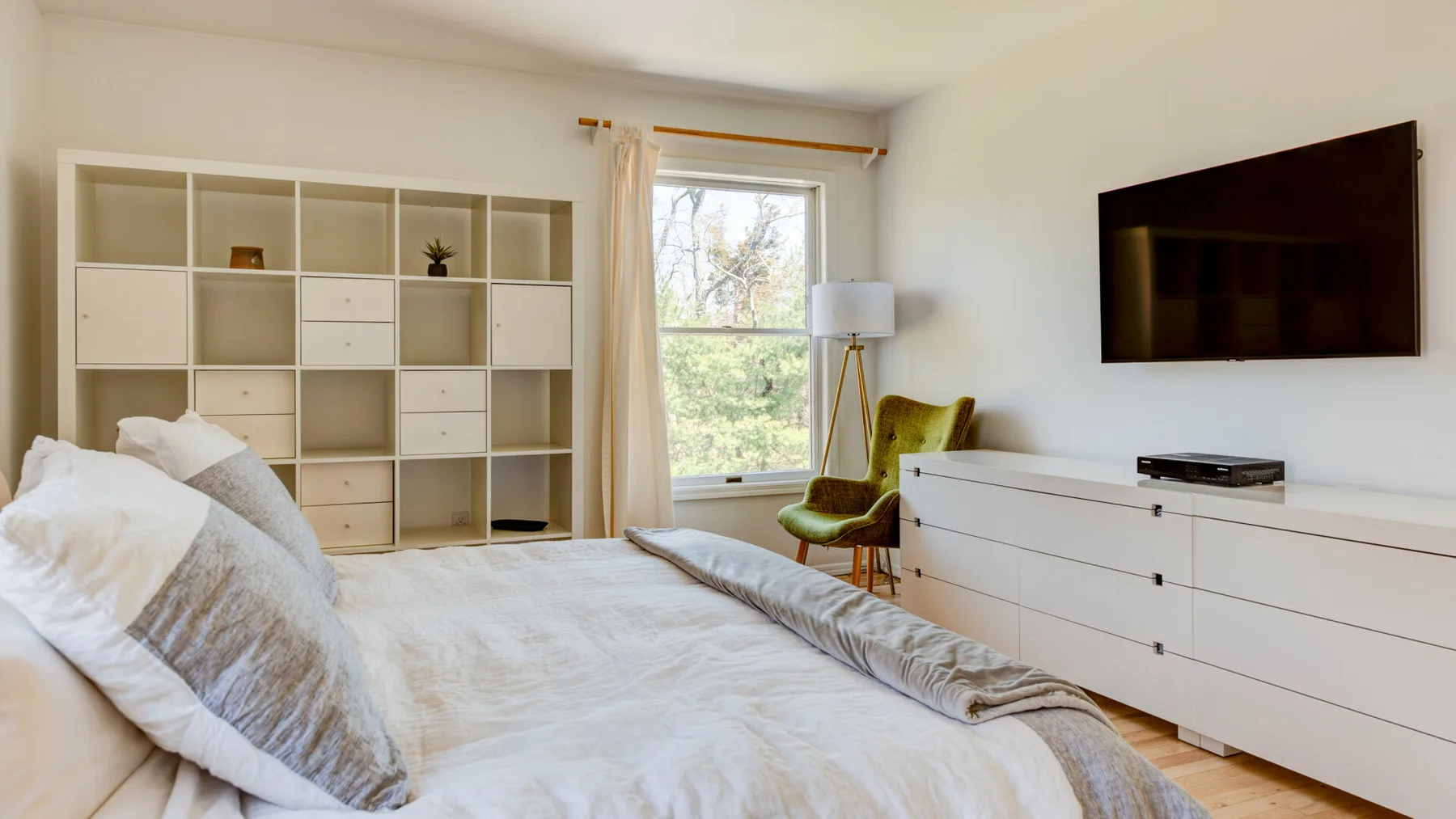 Un dormitorio luminoso con una cama, estantes empotrados y una ventana con vista a los árboles.