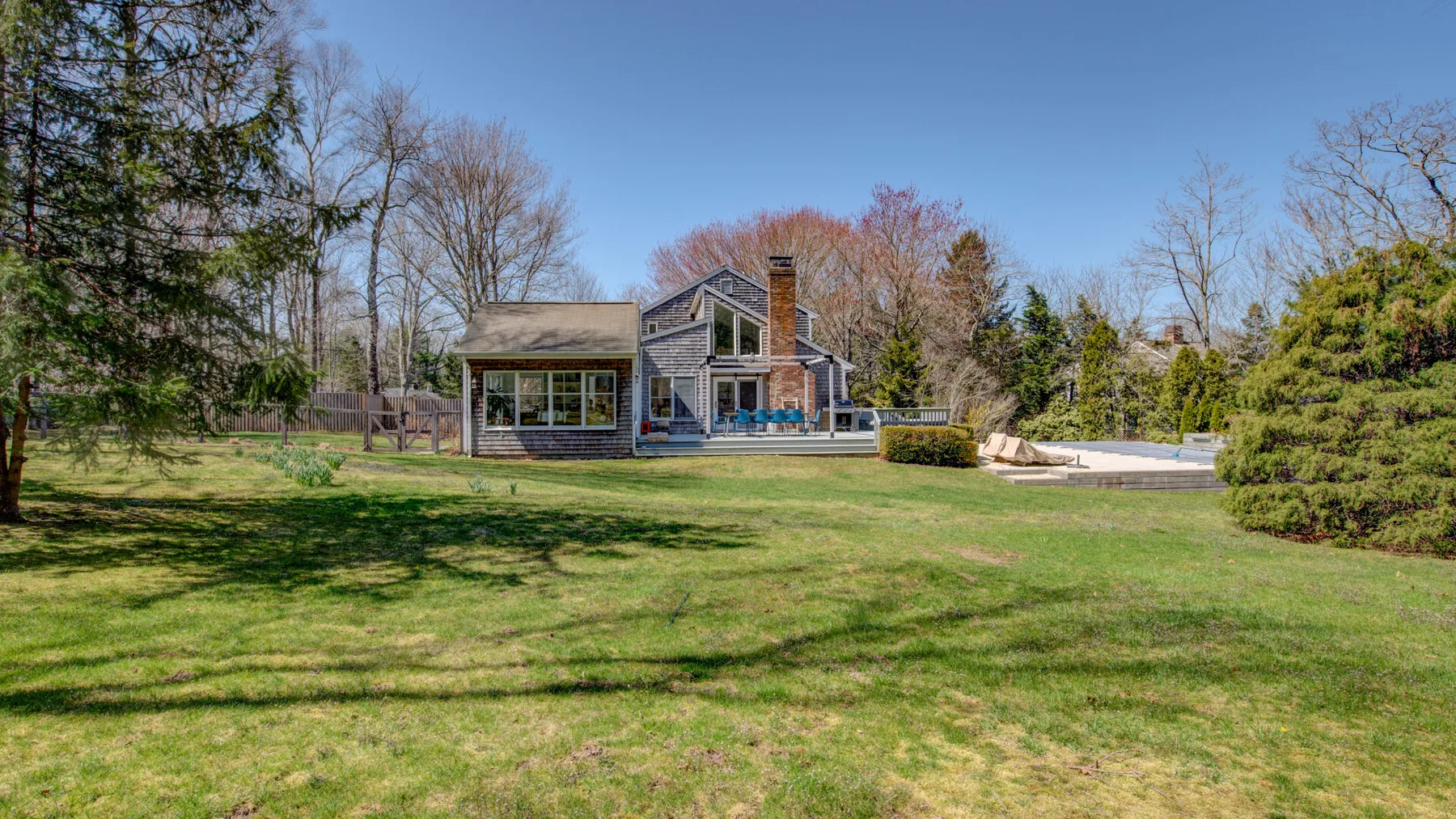 A house stands beyond a broad lawn, with trees and a pool nearby.