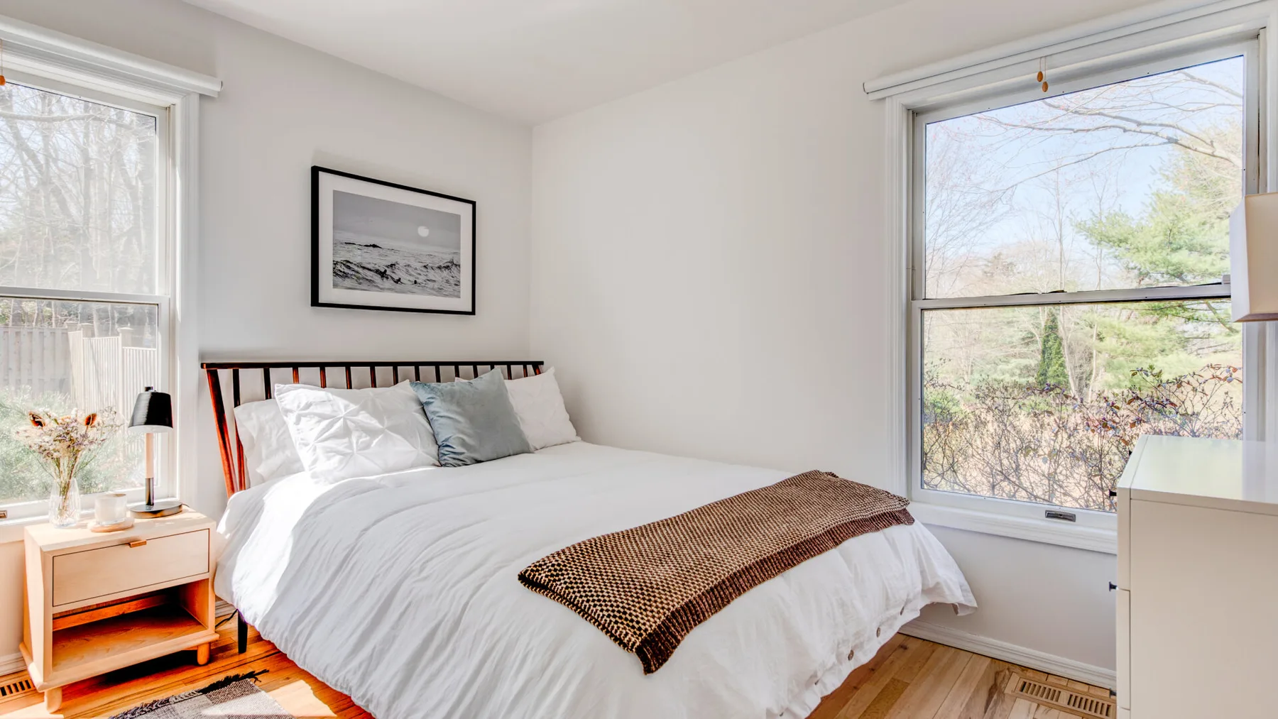 Un dormitorio luminoso con una cama bien tendida junto a grandes ventanas.