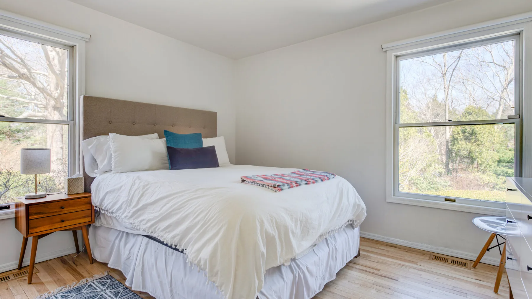 Un dormitorio luminoso con una cama entre dos ventanas grandes.
