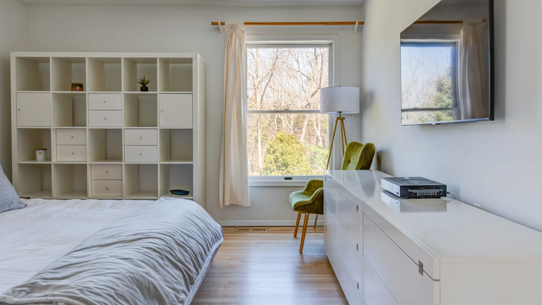 Un dormitorio luminoso con una cama, estanterías y un escritorio junto a la ventana.