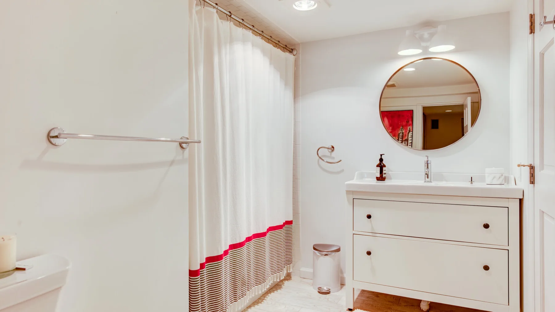 Un baño luminoso con tocador, espejo redondo y cortina de ducha.