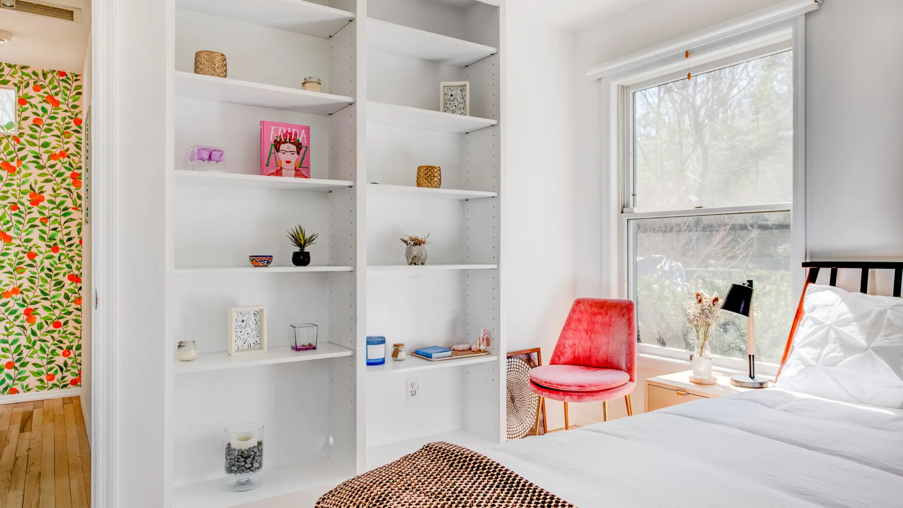 Un dormitorio luminoso con estantes empotrados y una cama junto a una ventana grande.