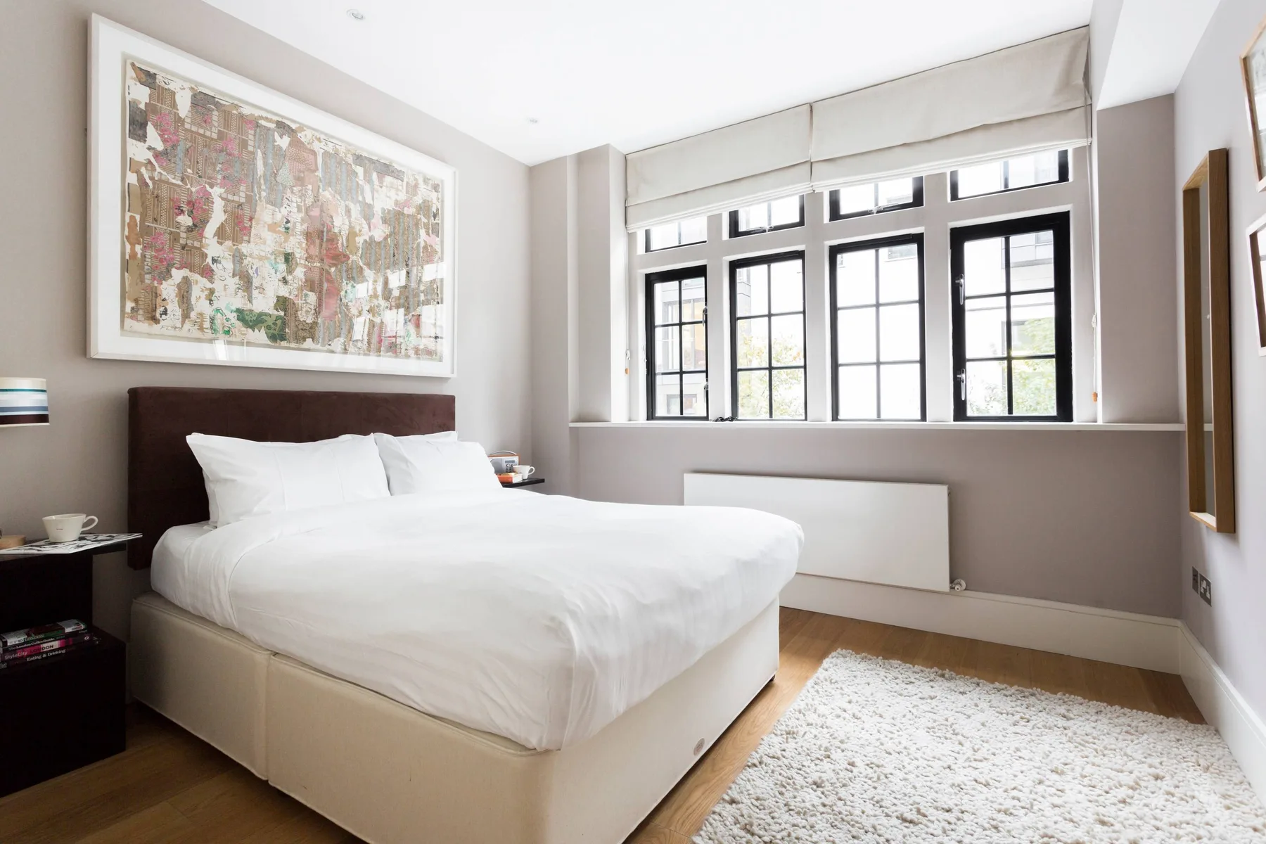 Un dormitorio luminoso con una cama junto a una hilera de ventanas grandes.
