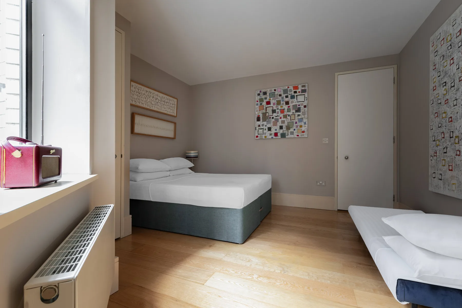 Un dormitorio con una cama, arte en las paredes y una ventana luminosa.