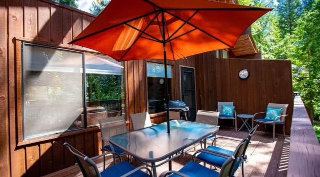 Un patio de madera con asientos al aire libre bajo una gran sombrilla naranja.