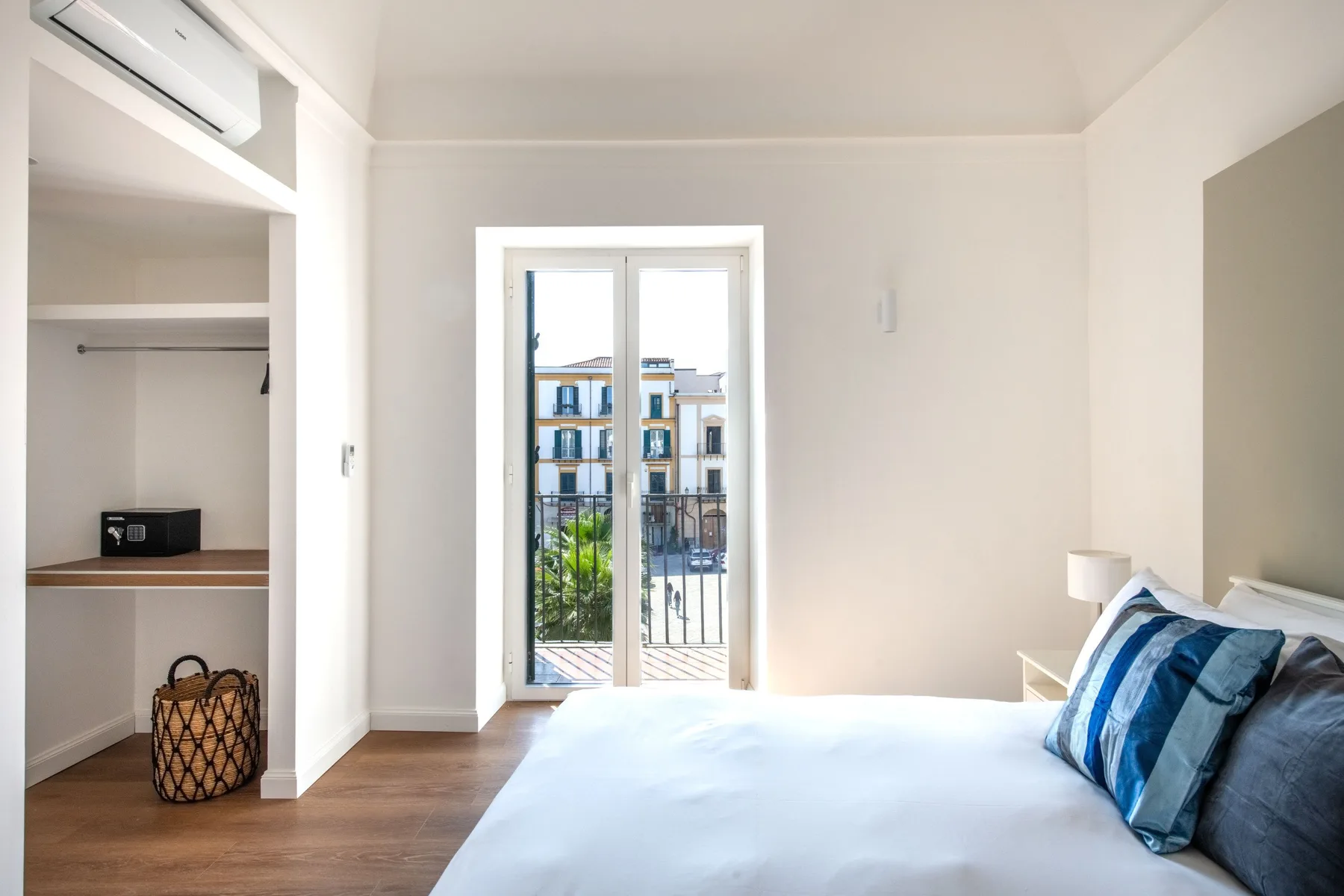 A bright bedroom with a bed beside open built-in shelving and a balcony door.