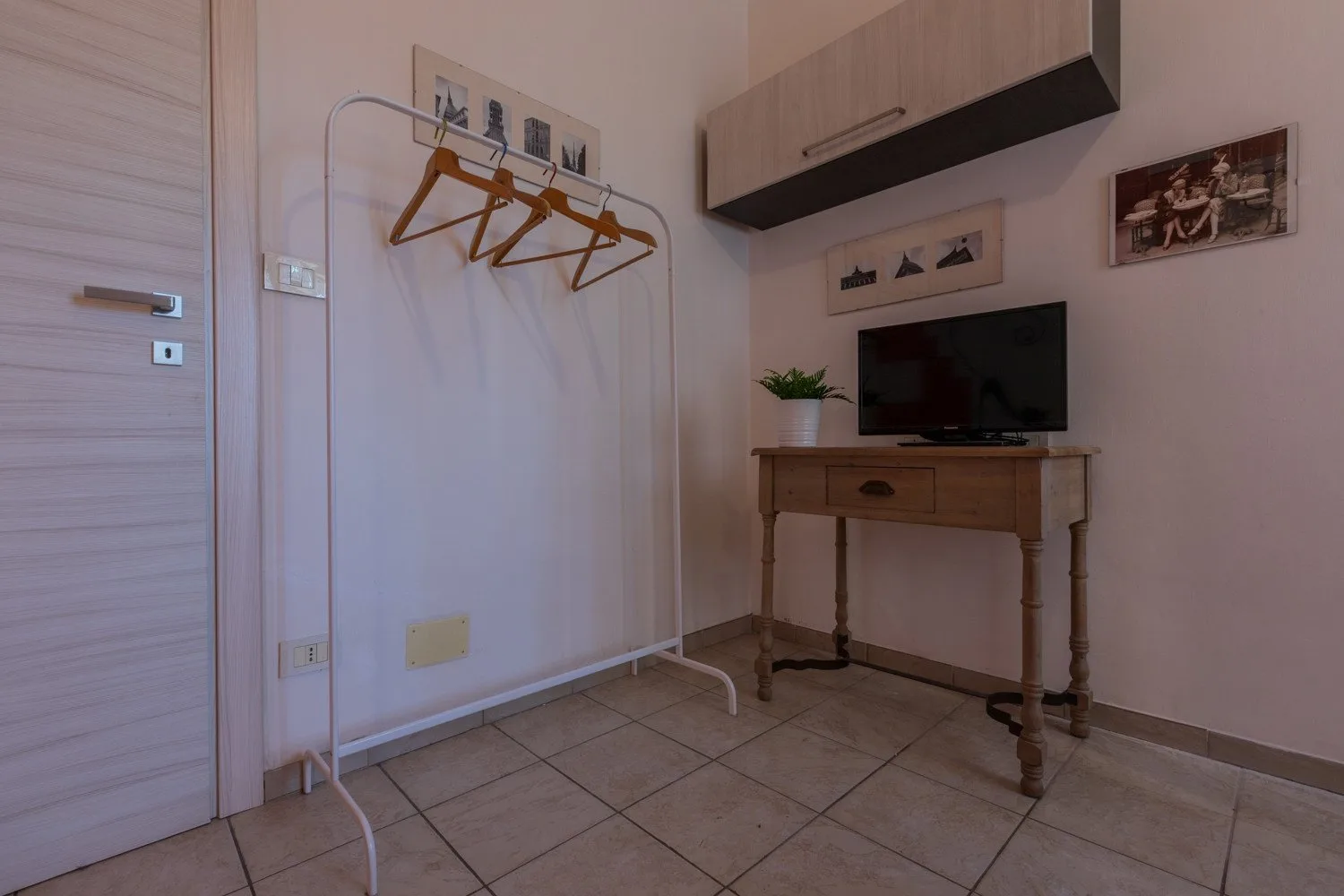 Una habitación con un perchero junto a una mesa pequeña y un televisor.
