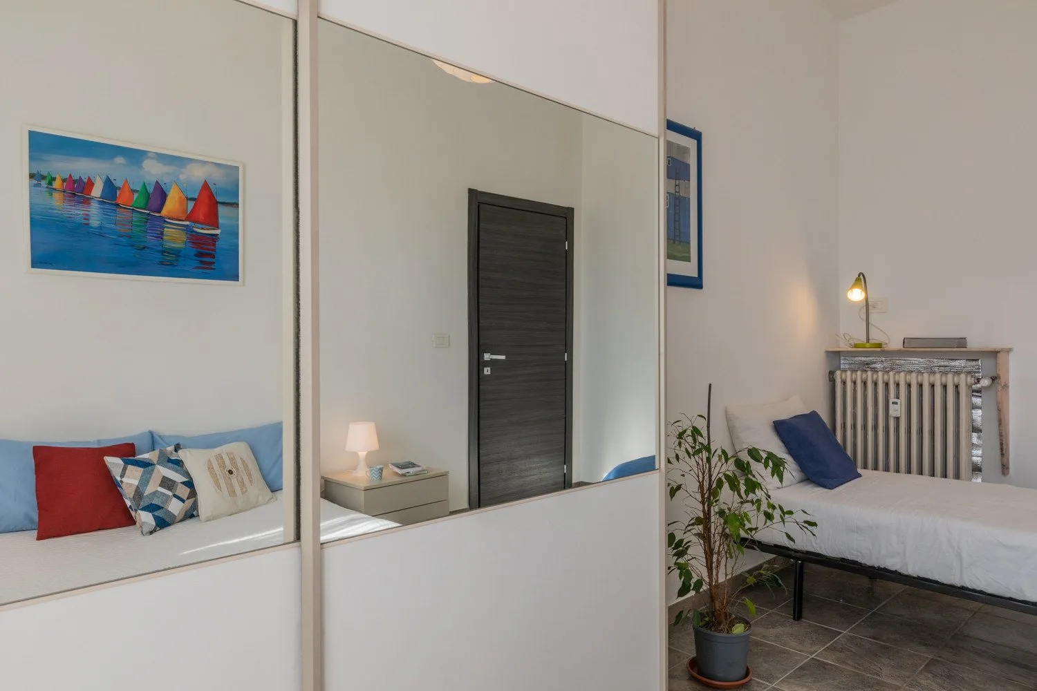 Un dormitorio con una cama, puertas de armario con espejos y un cuadro colorido de veleros.