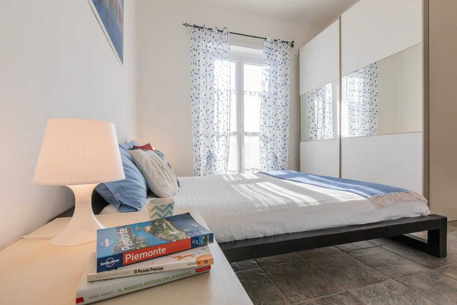 Un dormitorio con una cama bien tendida, cortinas estampadas y puertas de armario con espejo.