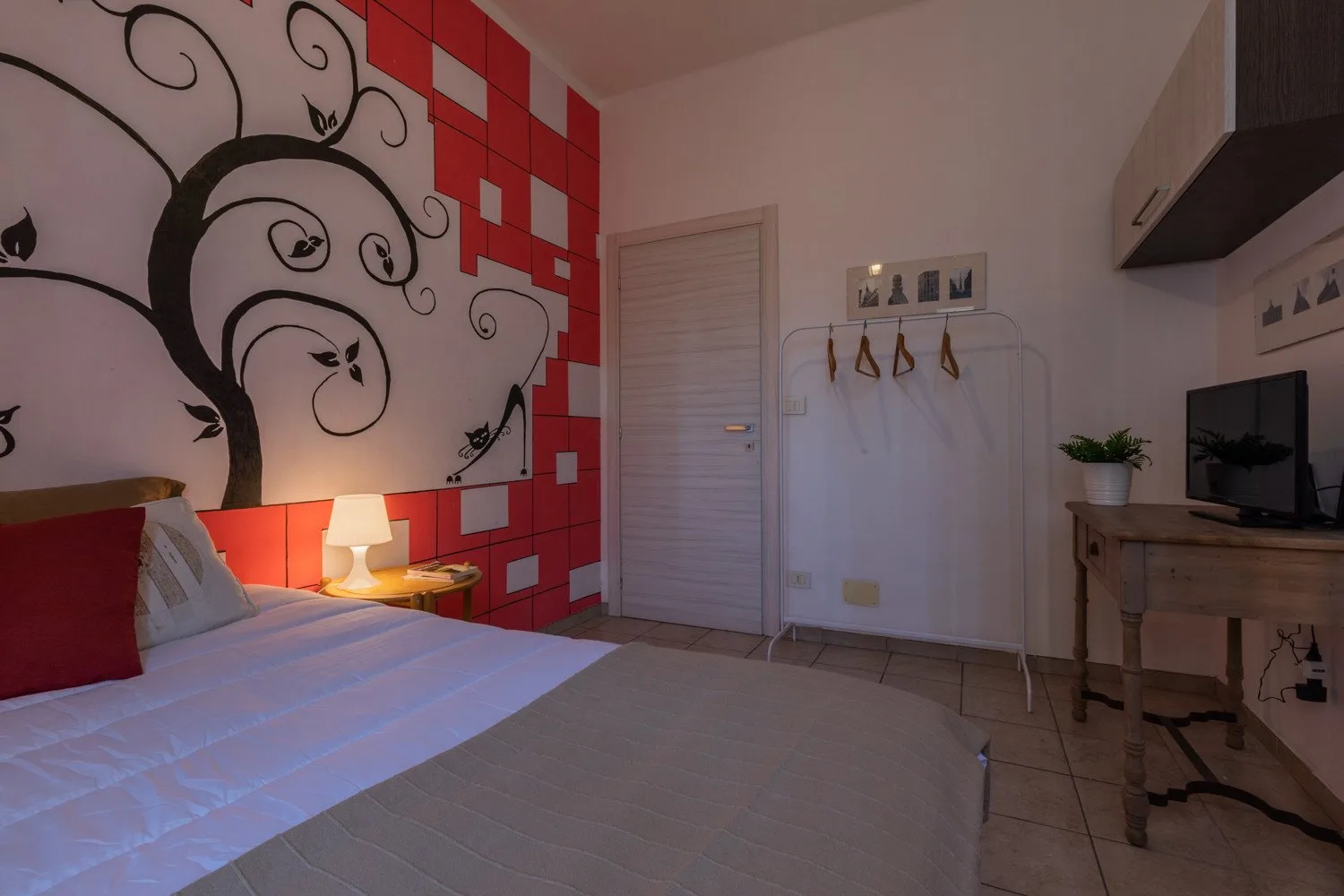 Un dormitorio con una cama, un mural decorativo en la pared y un pequeño escritorio con televisor.