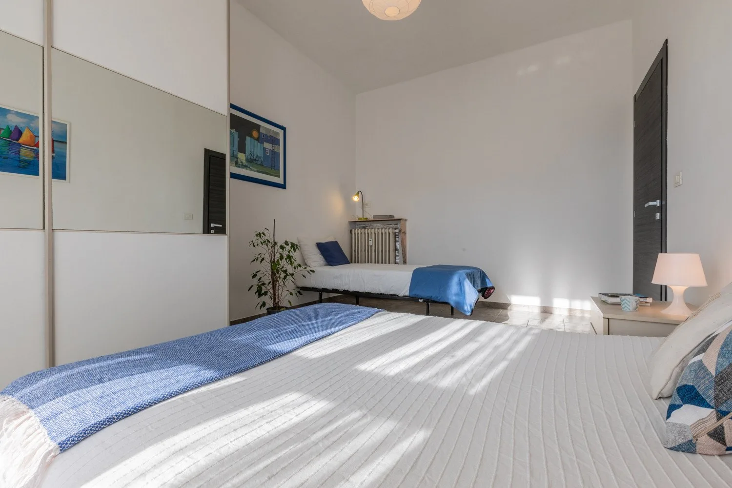 Un dormitorio luminoso con camas, ropa de cama azul y cuadros en las paredes.
