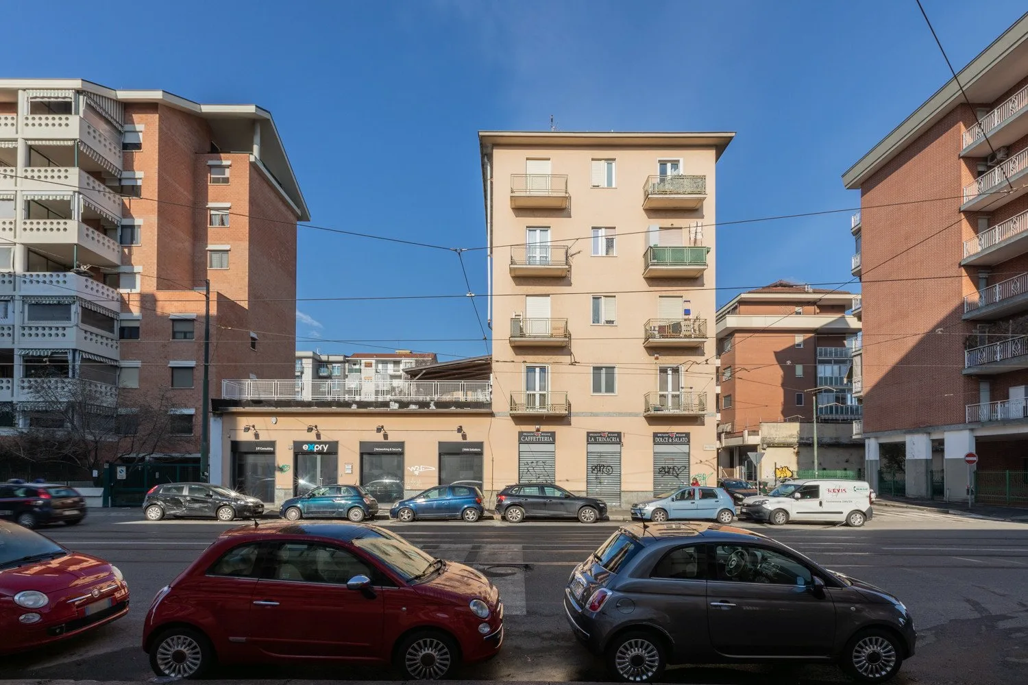 Una calle urbana con coches estacionados frente a varios edificios de apartamentos.