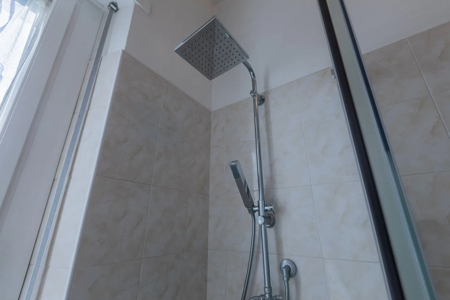 Una ducha alicatada con un cabezal superior grande y una ducha de mano.