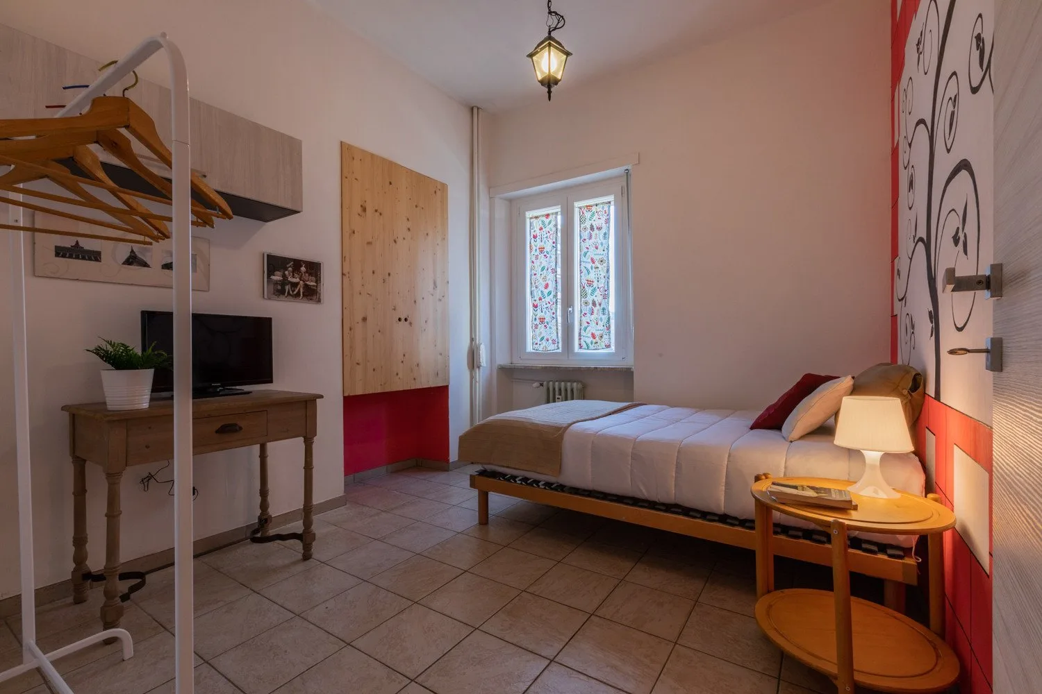 Un dormitorio con una cama junto a una ventana y una mesita con una lámpara.