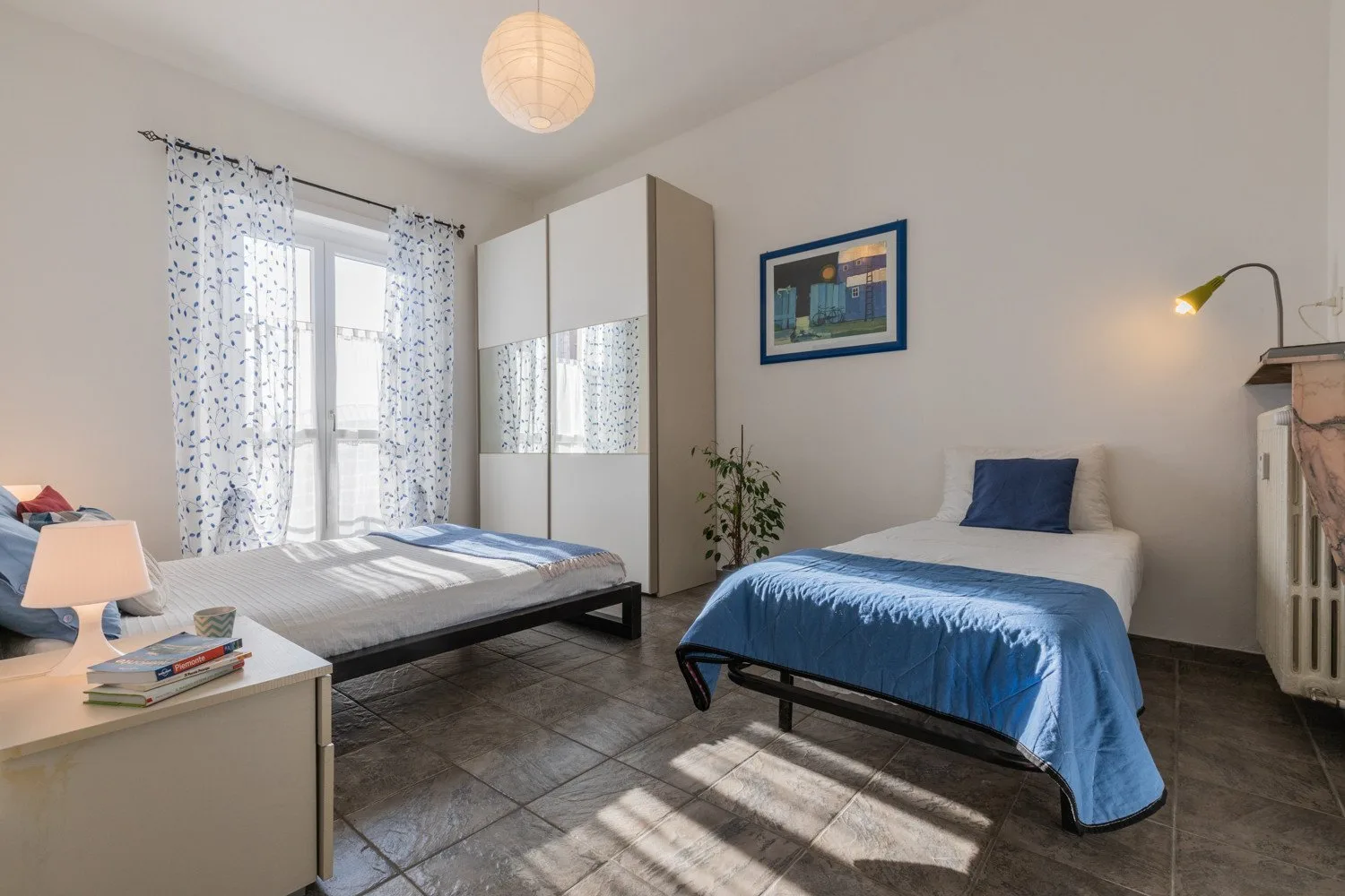 Un dormitorio con dos camas, un armario y una ventana con cortinas estampadas.