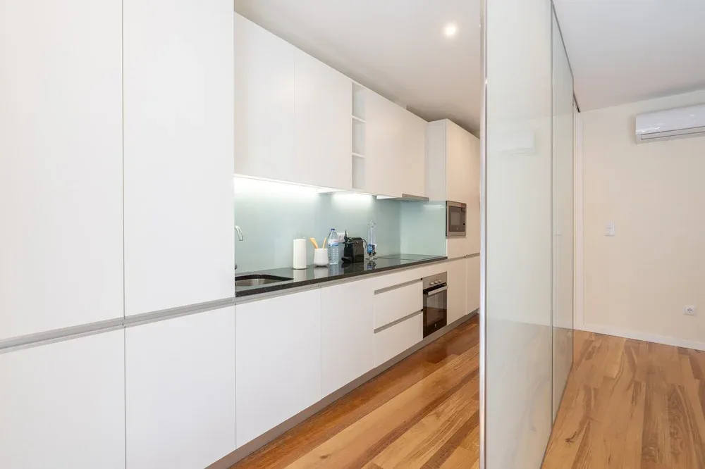 A modern kitchen with white cabinets, a dark countertop, and wood flooring.
