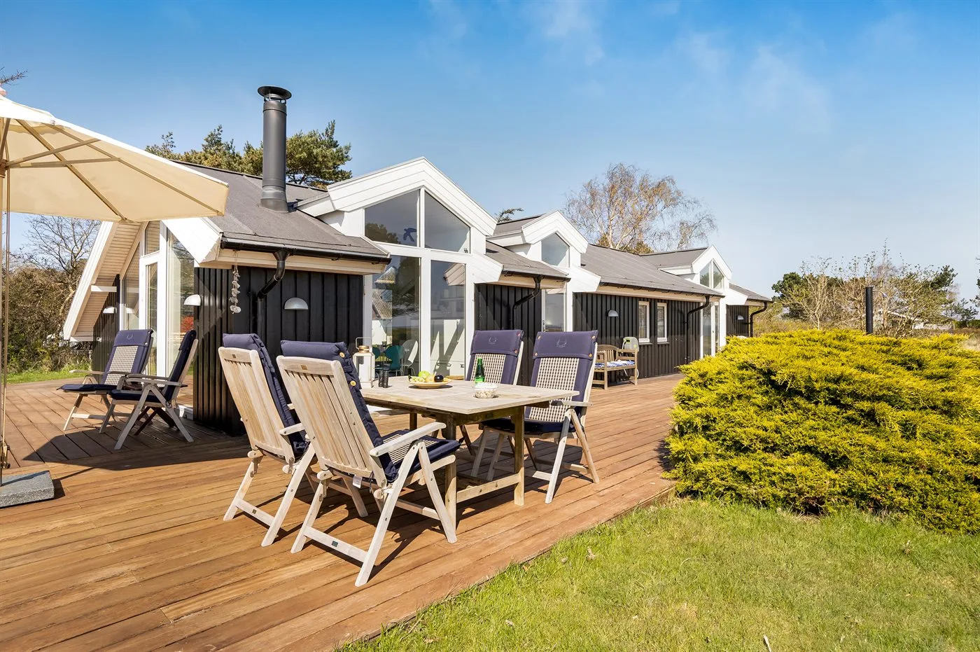 Una casa con una terraza de madera, asientos al aire libre y una sombrilla grande.