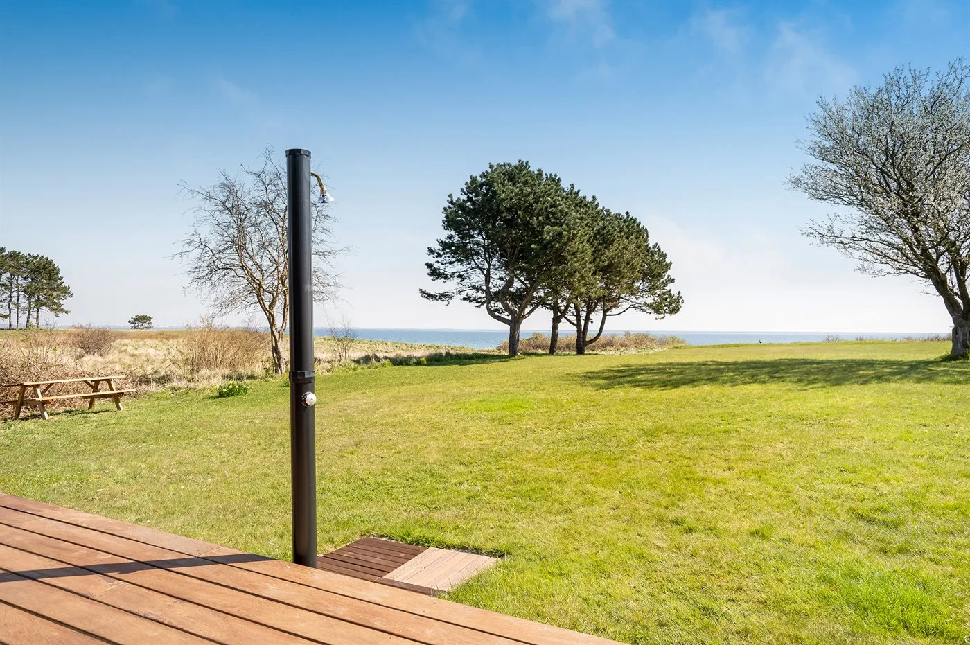 Zona exterior con césped, árboles, una mesa de picnic y una terraza de madera junto al agua.