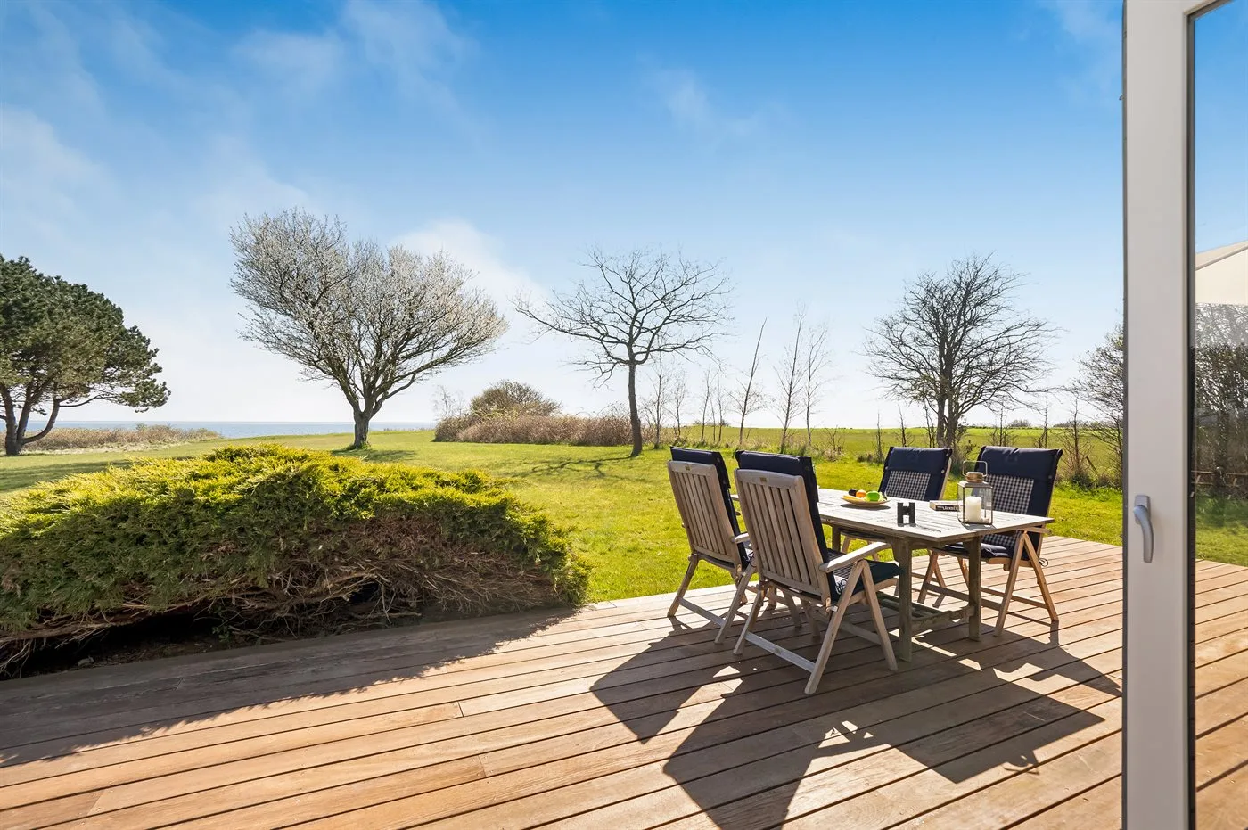 Una terraza de madera con asientos al aire libre da a un paisaje de césped y árboles.