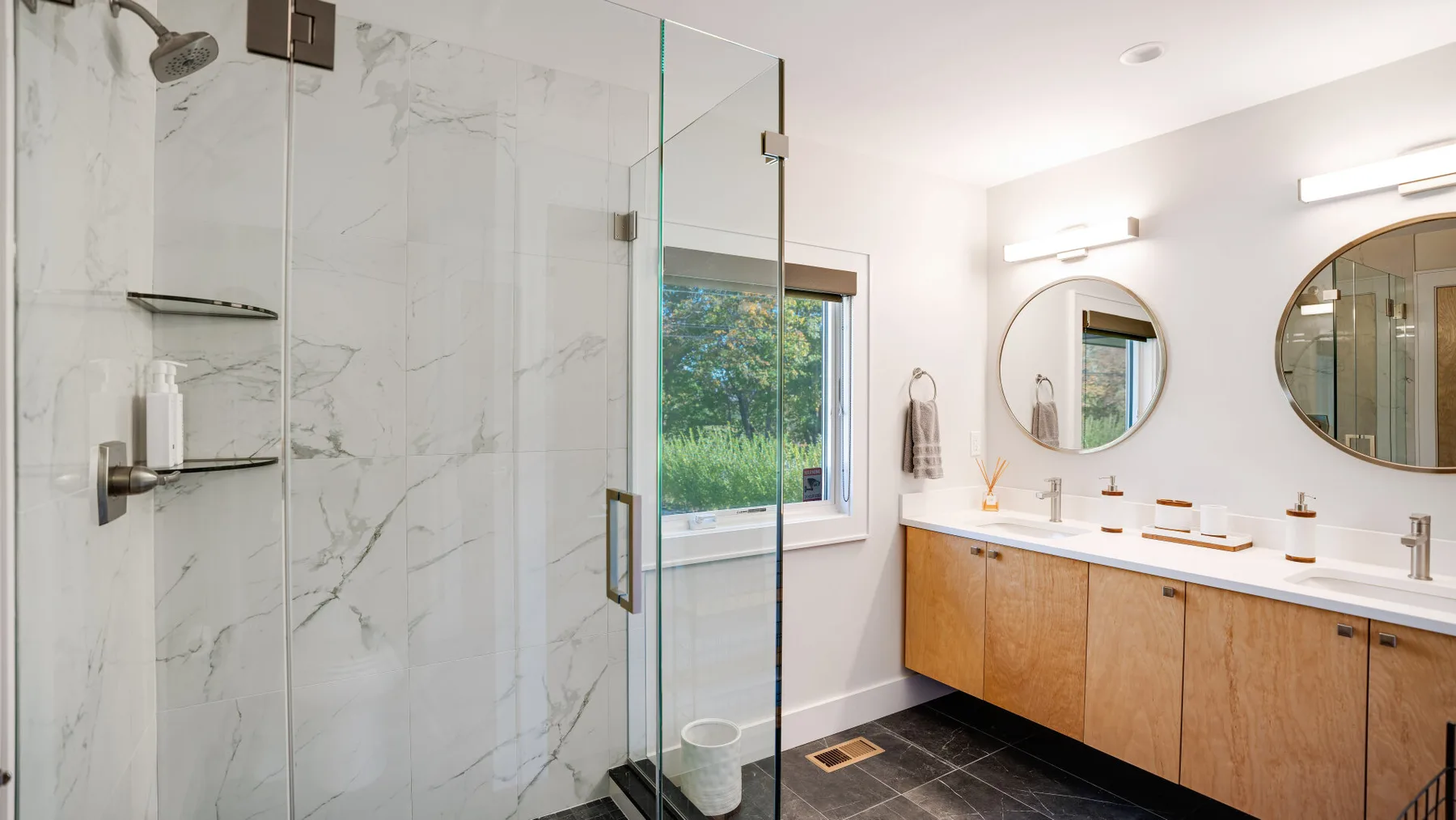 Un baño luminoso con ducha de vidrio, lavabo doble y mueble de tono madera.