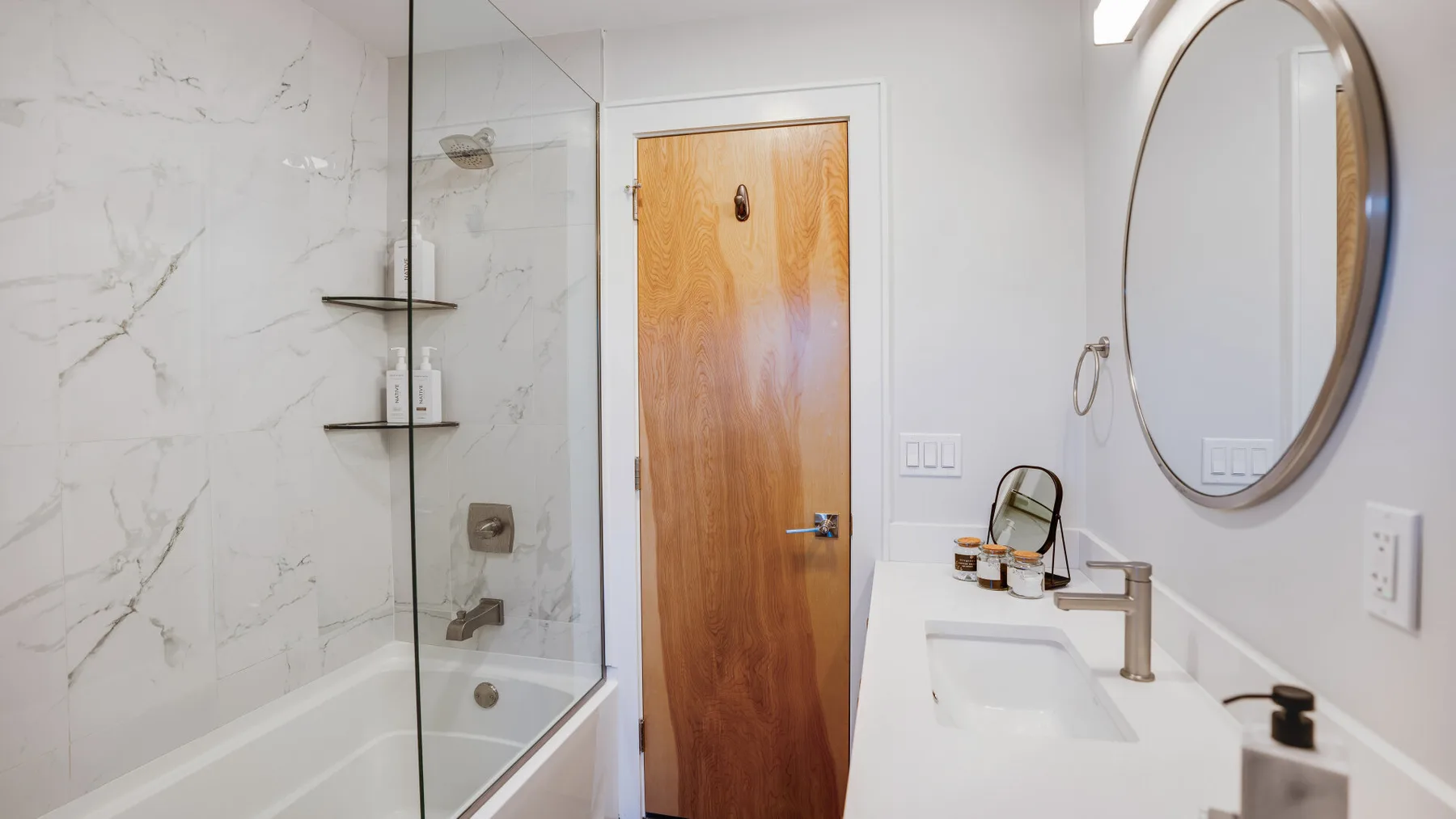 Un baño luminoso con bañera, mampara de vidrio y lavabo.