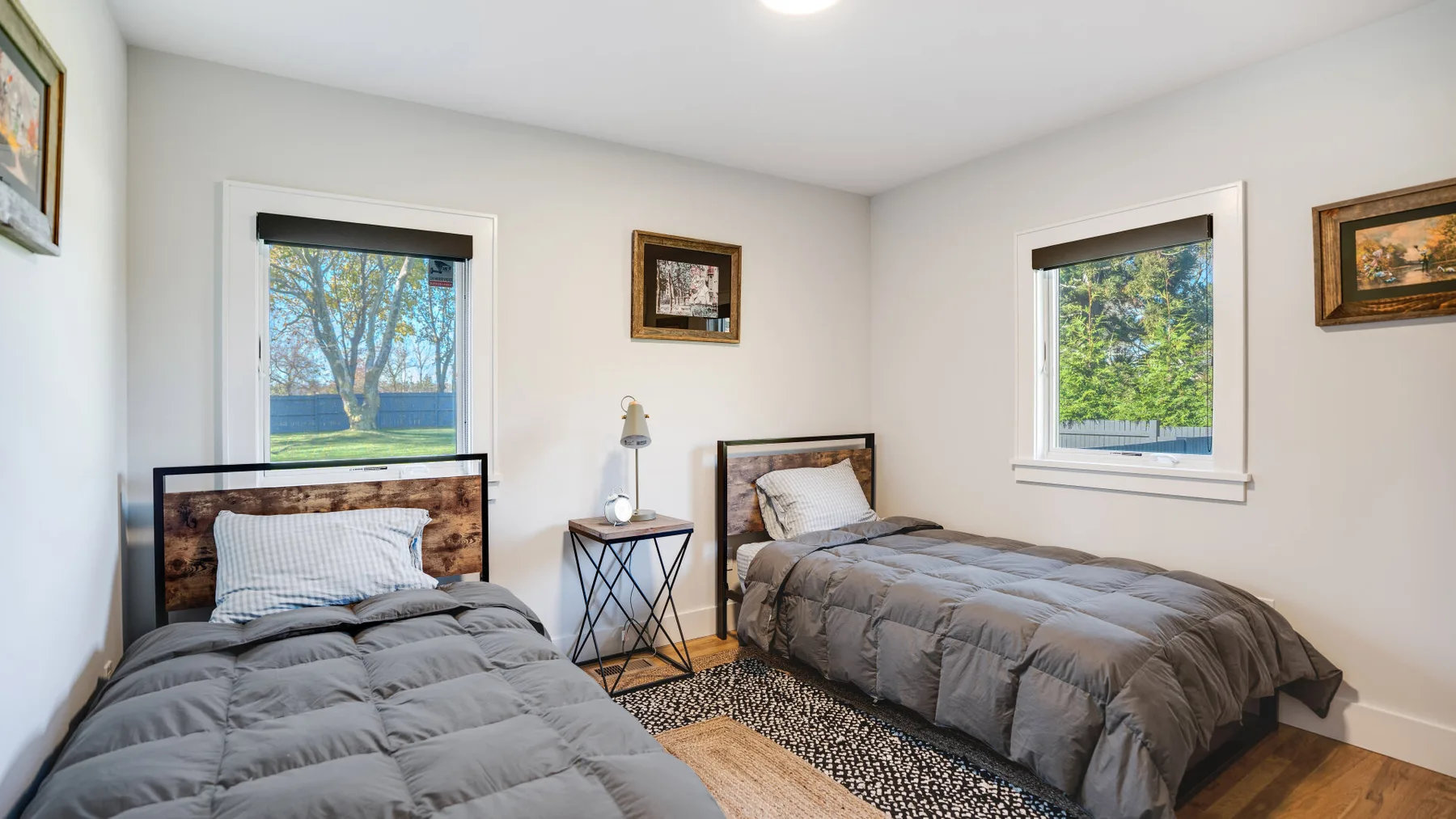 A bedroom with two single beds, bedside tables, and windows overlooking greenery.
