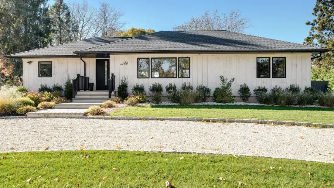 A single-story house with a dark roof stands behind a gravel driveway.