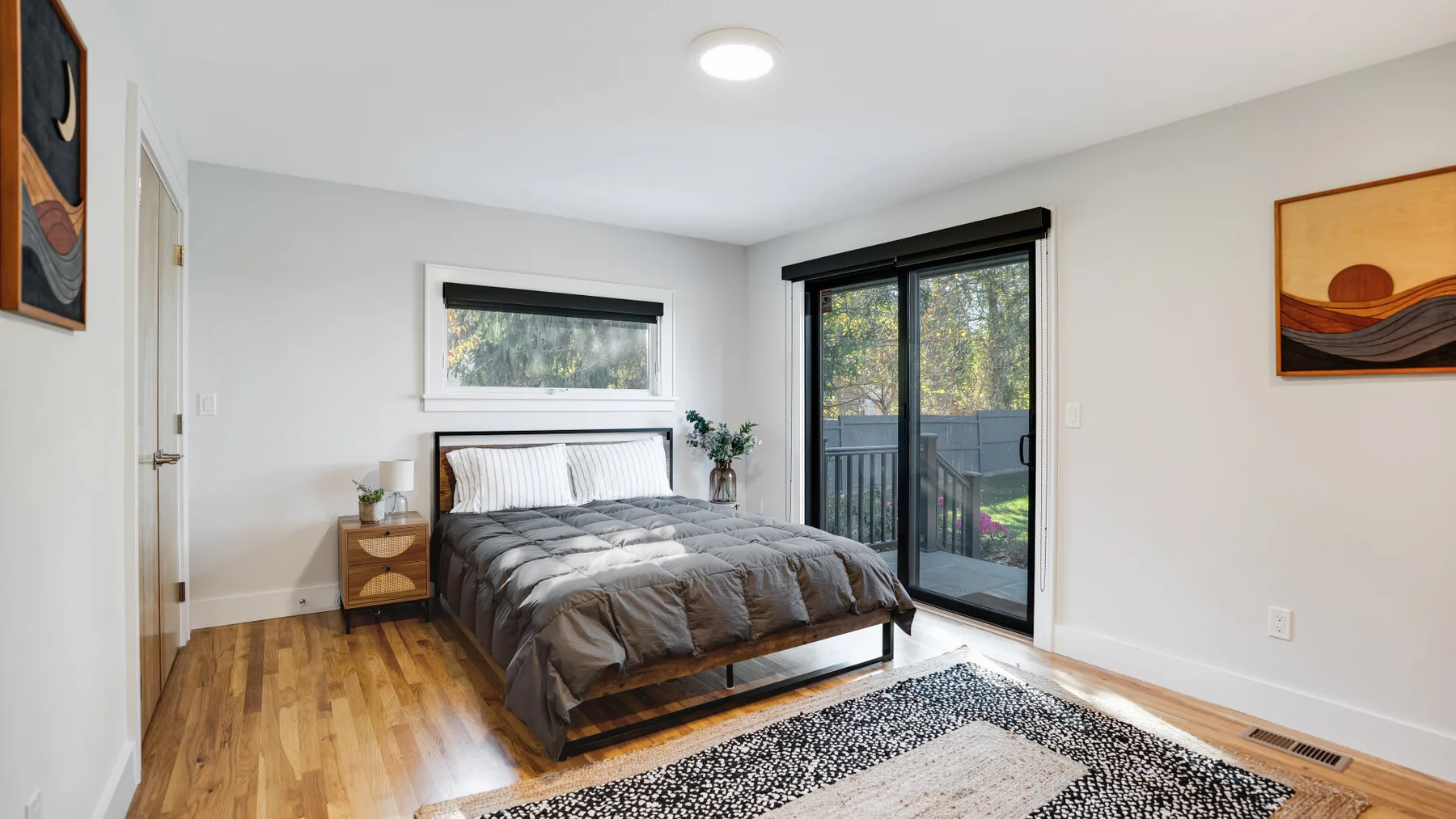Un dormitorio luminoso con una cama, suelo de madera y una puerta grande de cristal.