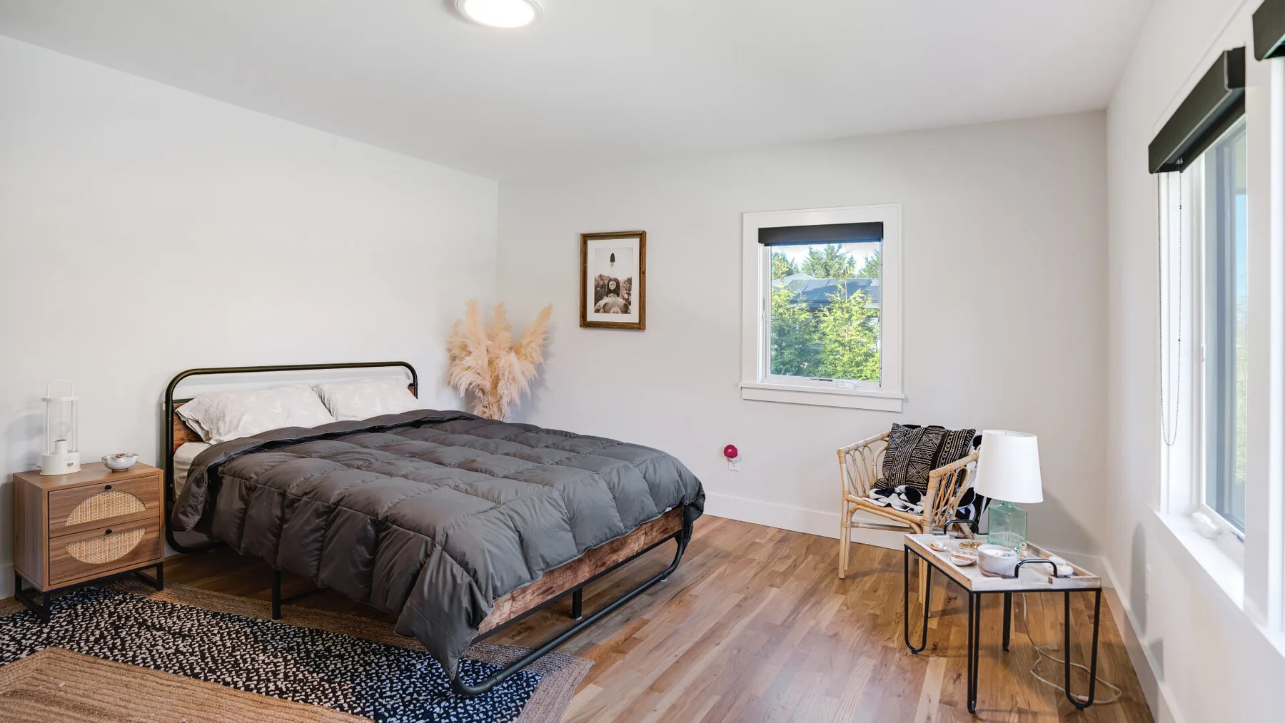 A bright bedroom with a bed, bedside table, and large windows.