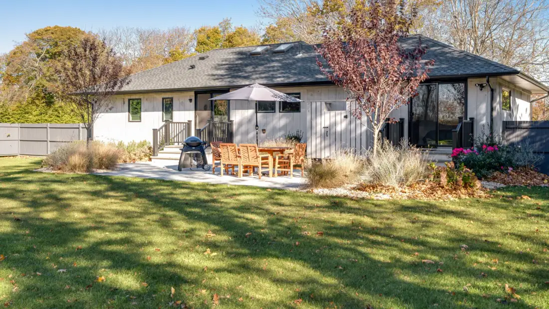 A single-story house opens onto a lawn with a patio seating area.