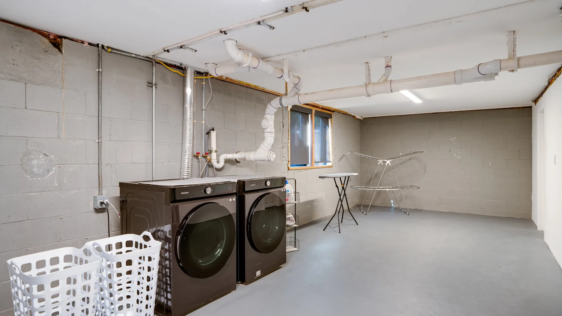 A basement laundry room with two washing machines and laundry baskets.