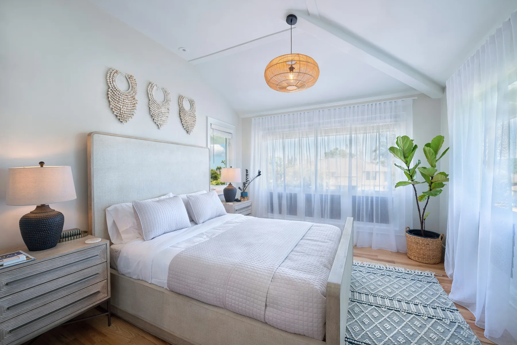 Un dormitorio luminoso con una cama tendida y cortinas translúcidas en la ventana.
