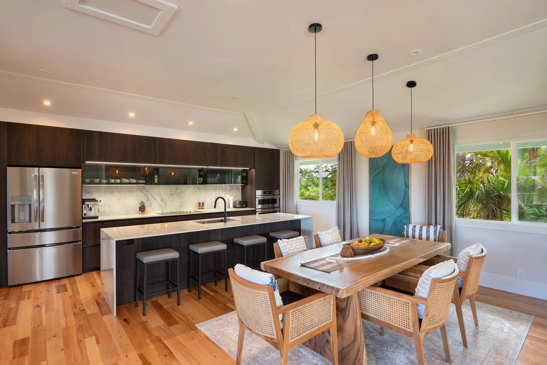 Una cocina abierta y zona de comedor con una larga mesa de madera bajo lámparas colgantes.