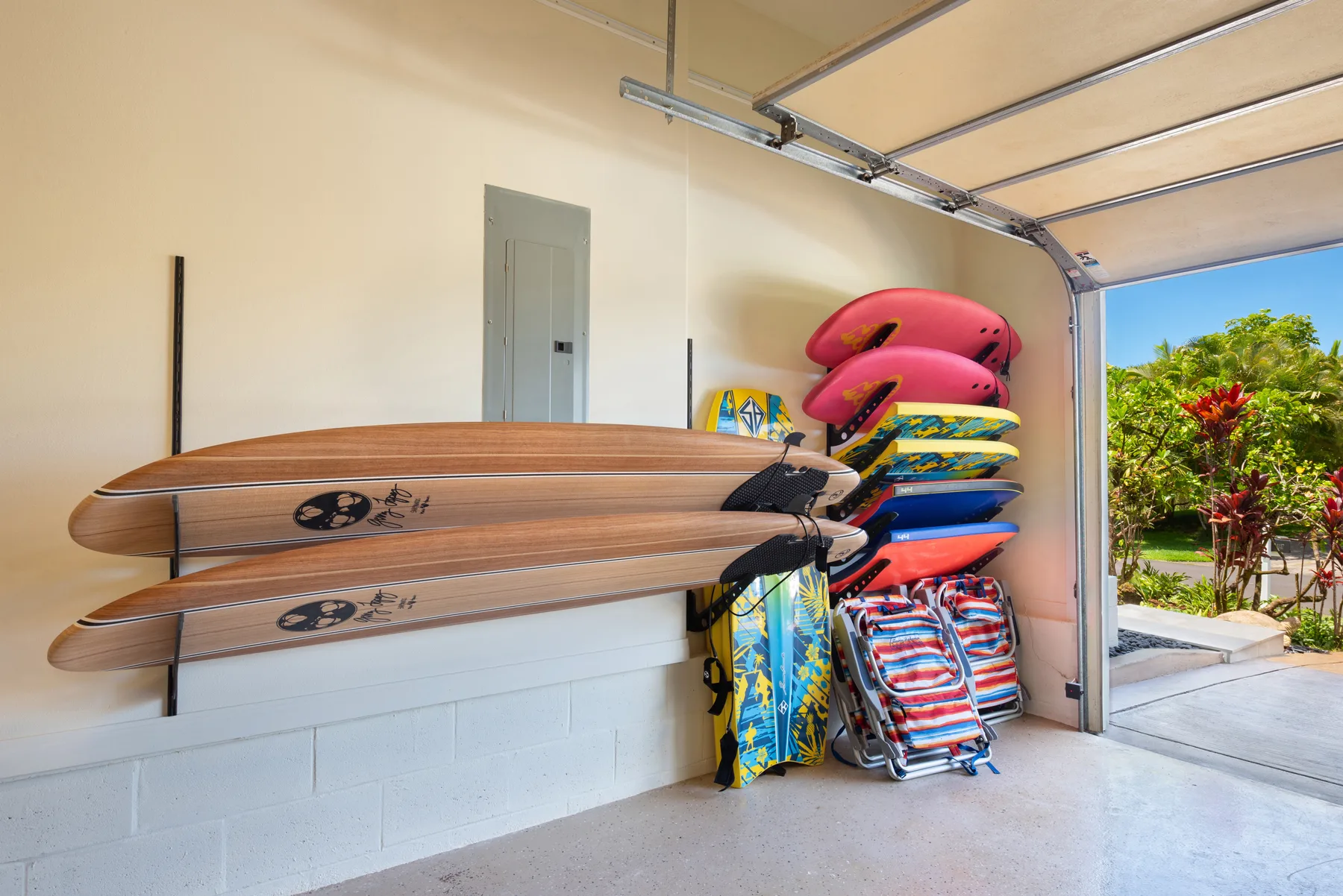 Zona de almacenamiento en un garaje con tablas de surf, flotadores coloridos y sillas de playa plegadas.