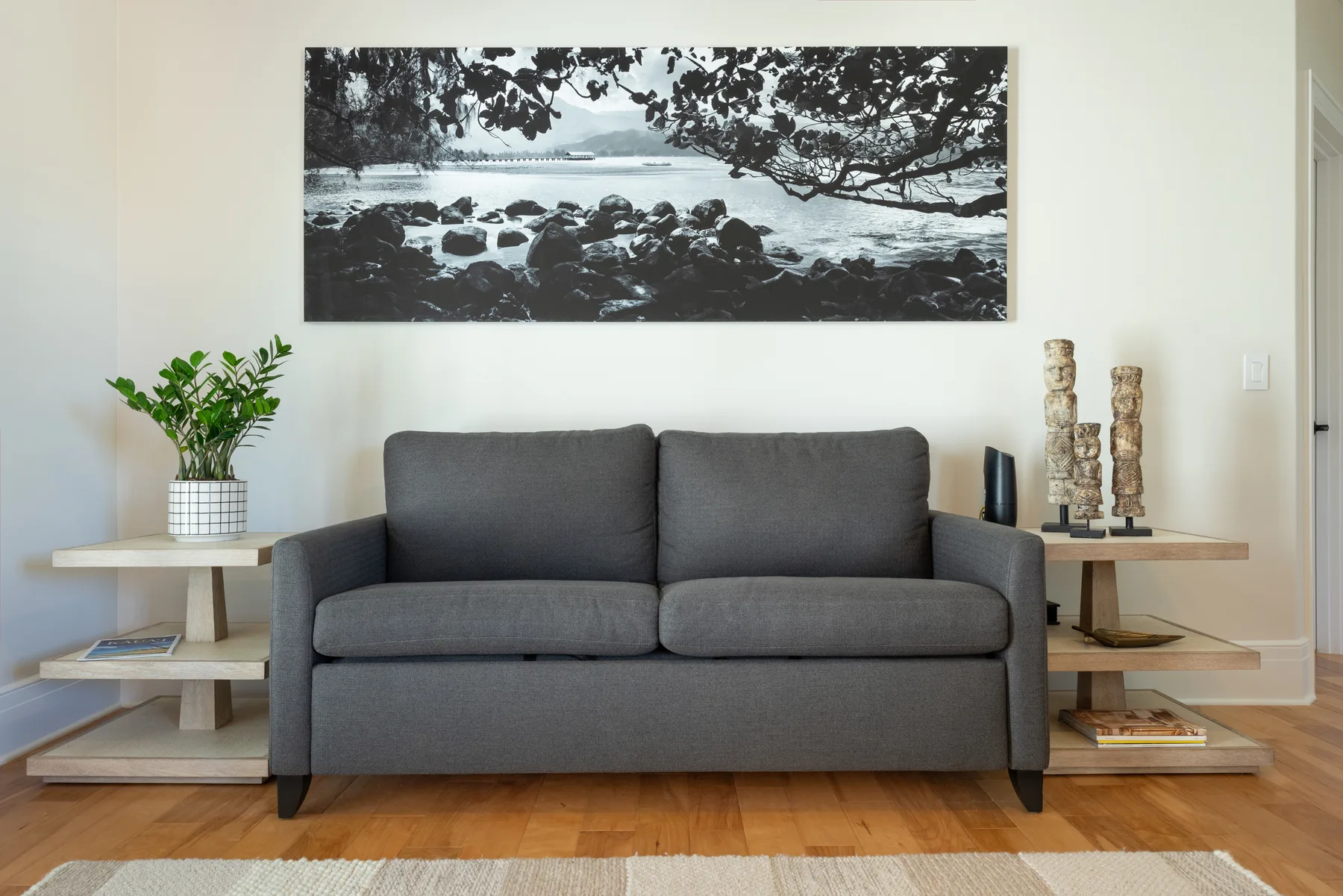 Una sala de estar con asientos grises bajo una amplia fotografía de paisaje en blanco y negro.
