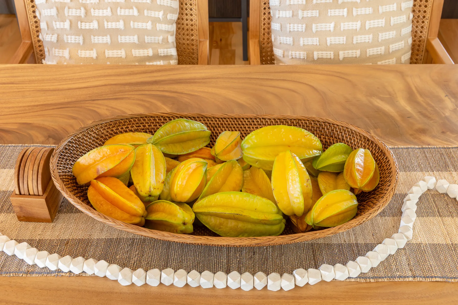 Una mesa de madera sostiene un cuenco tejido con frutas amarillas y verdes.
