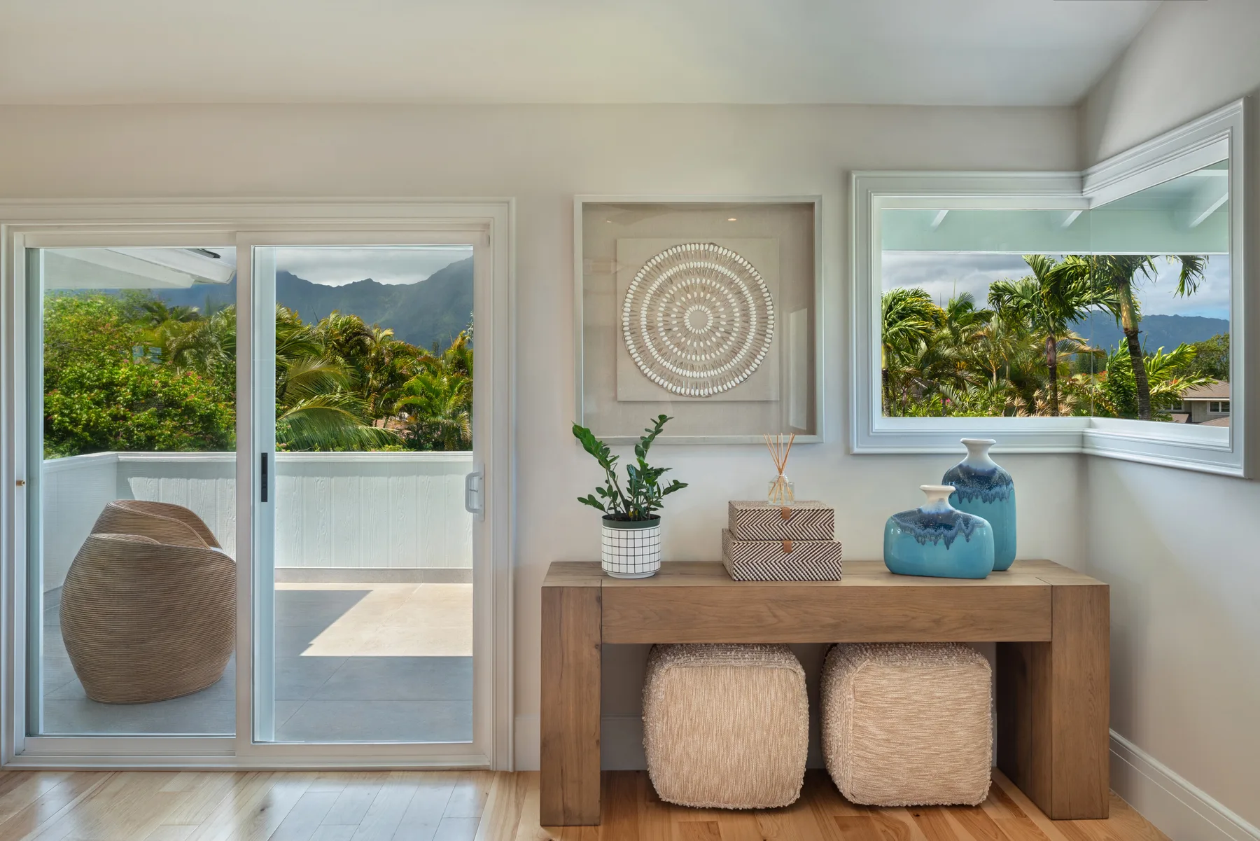 Una habitación luminosa con una consola de madera, asientos tejidos y ventanas con vistas a vegetación tropical.