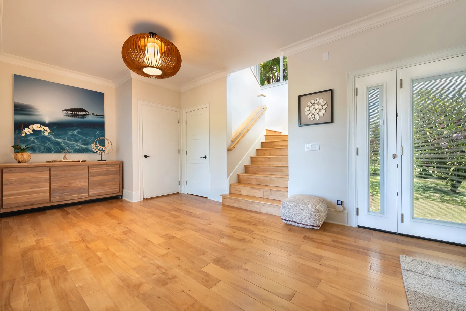 Una entrada luminosa con escaleras de madera, un aparador y puertas de vidrio.
