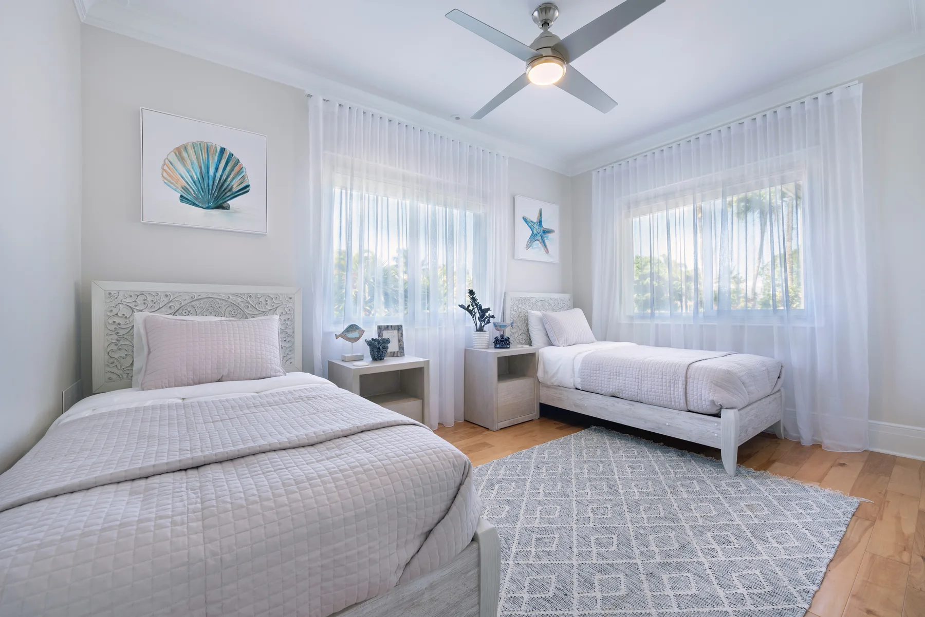 Un dormitorio luminoso con dos camas, cortinas translúcidas y una alfombra estampada.