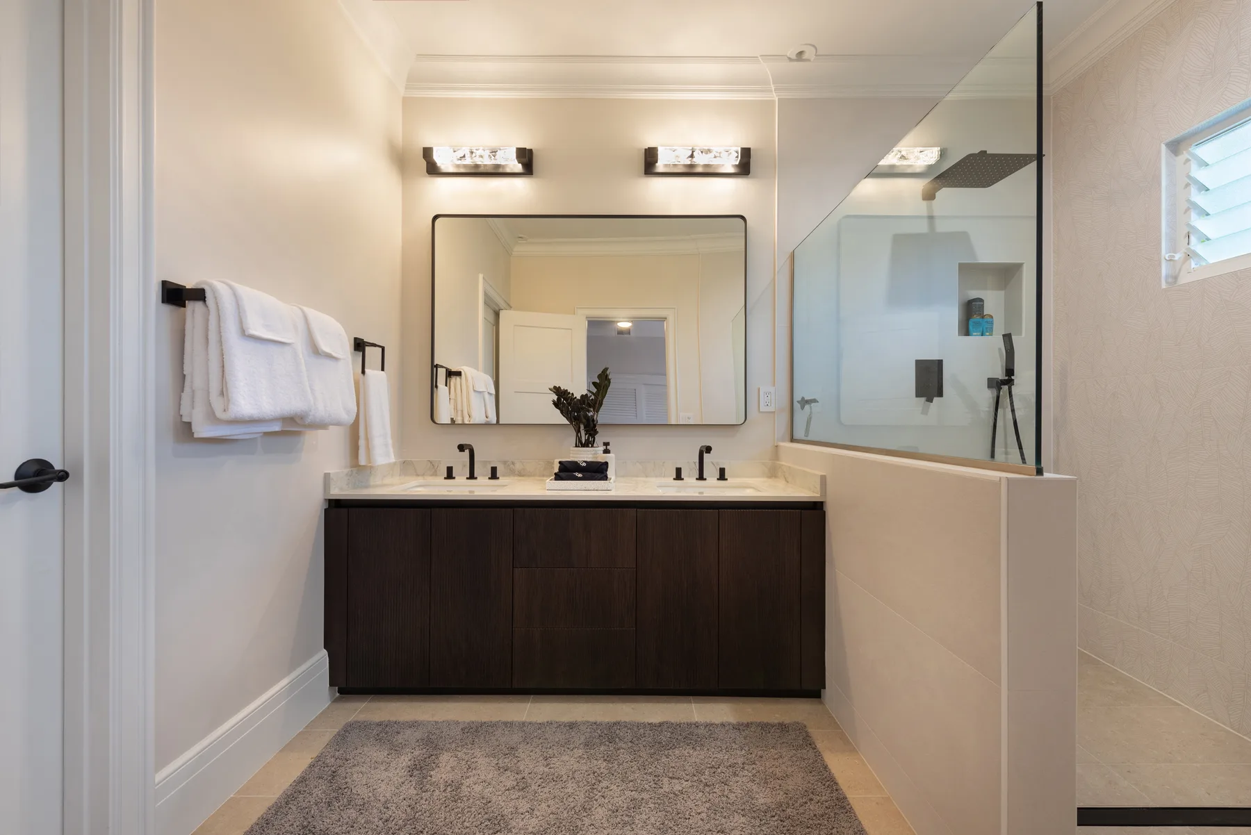 Un baño luminoso con lavabo doble, un espejo grande y una ducha de vidrio.