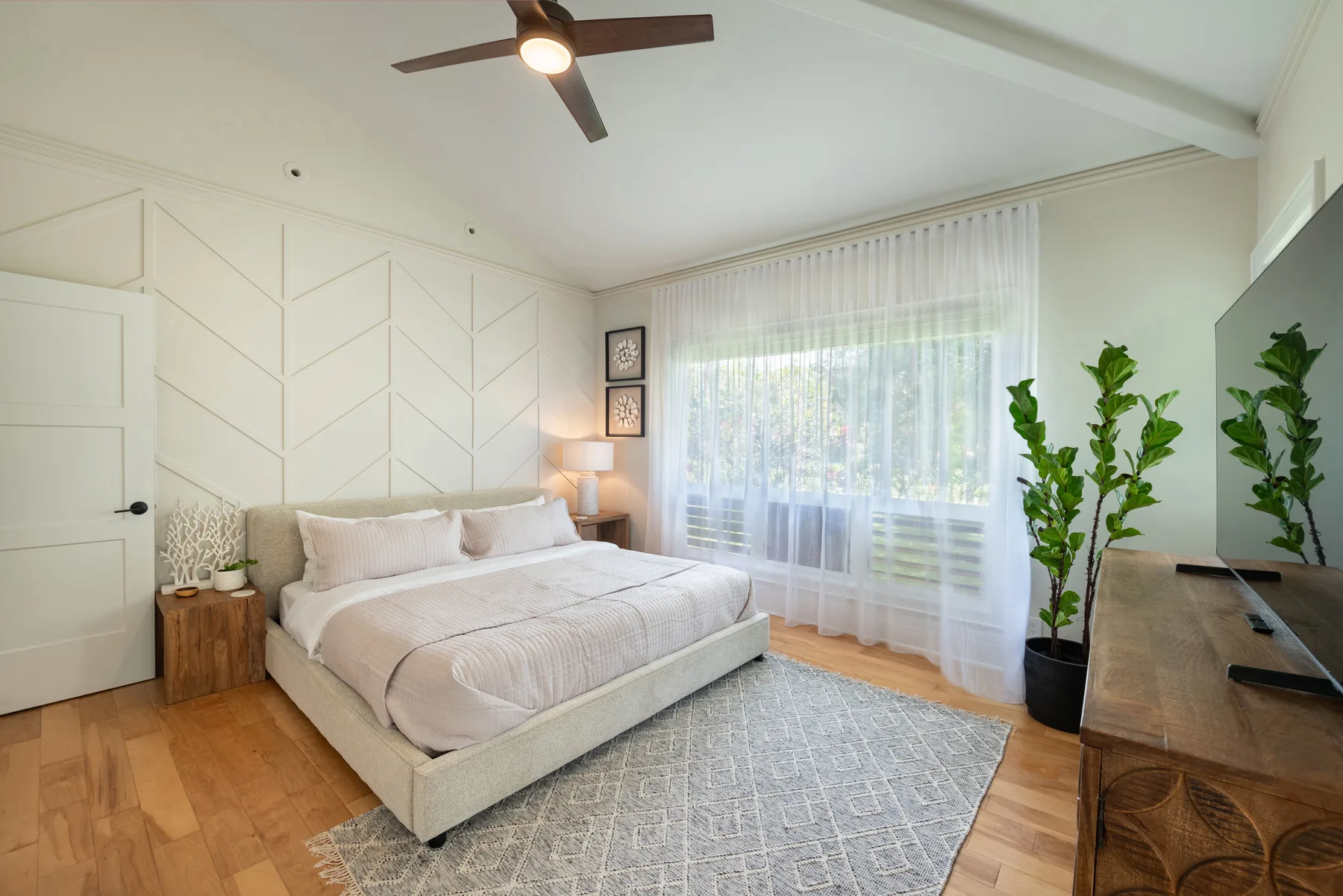 Un dormitorio luminoso con una cama, una gran ventana con cortinas y plantas en macetas.
