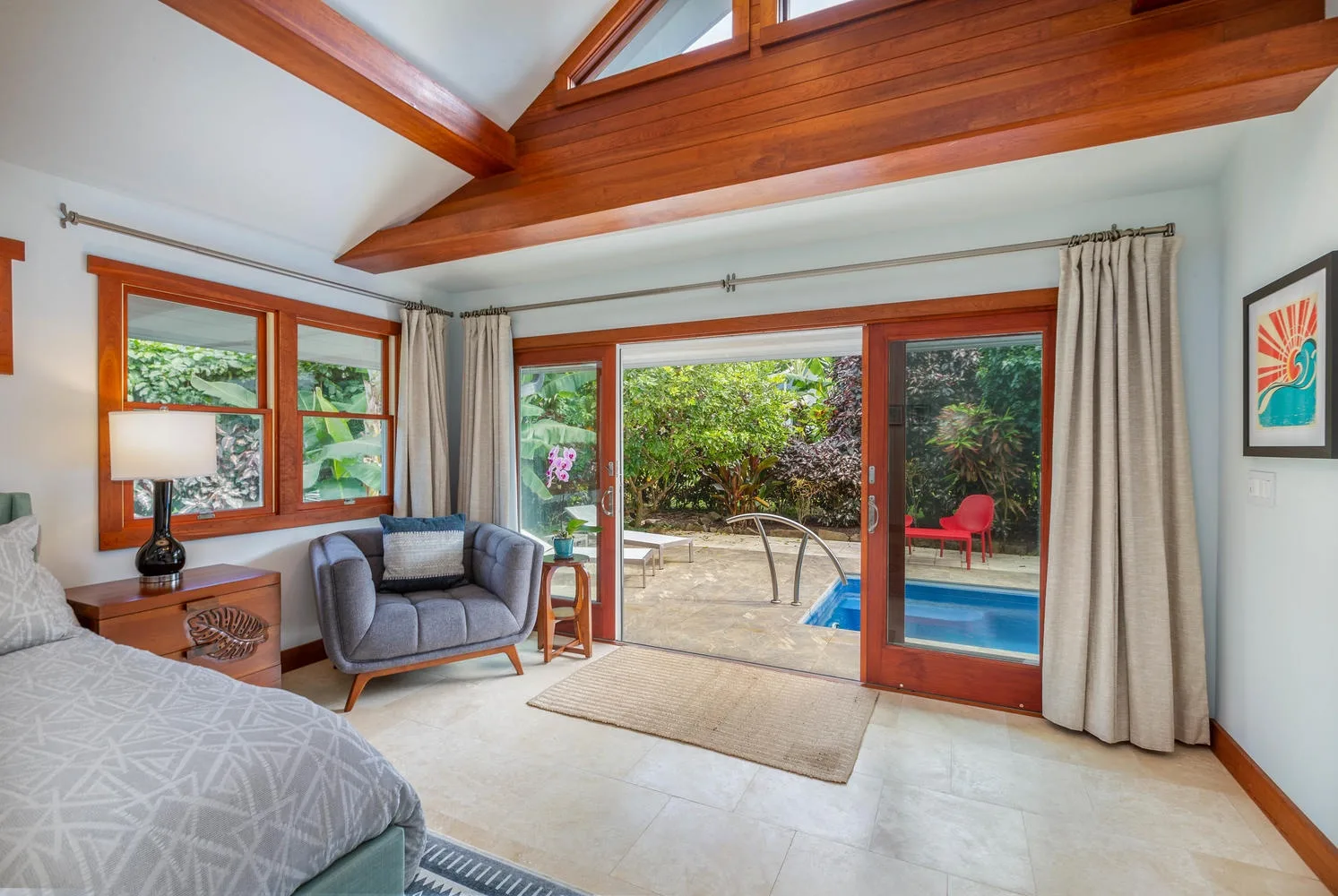 A bright bedroom opens through sliding glass doors to a garden and pool.