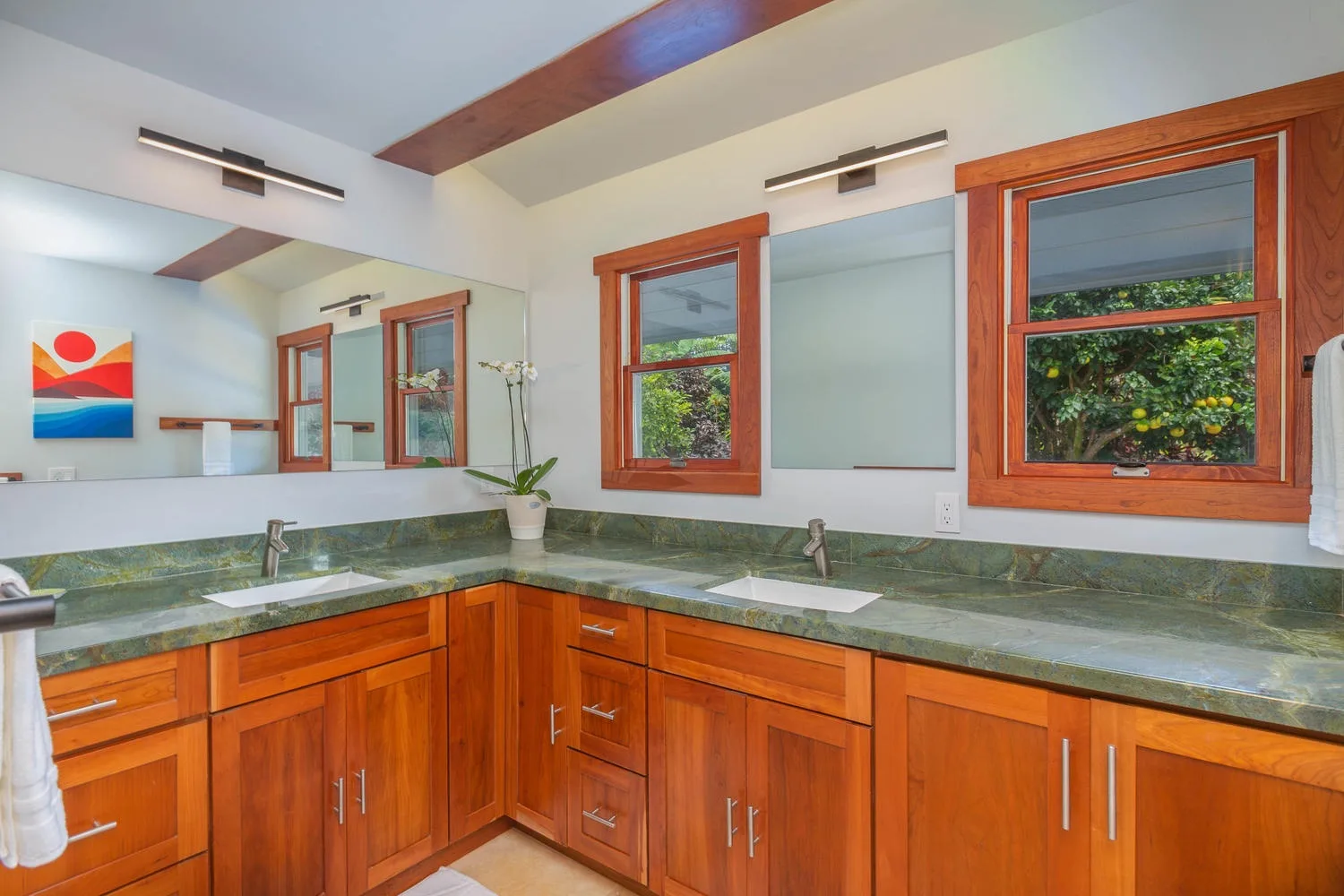 A bright bathroom vanity with wooden cabinets, green countertops, and windows.