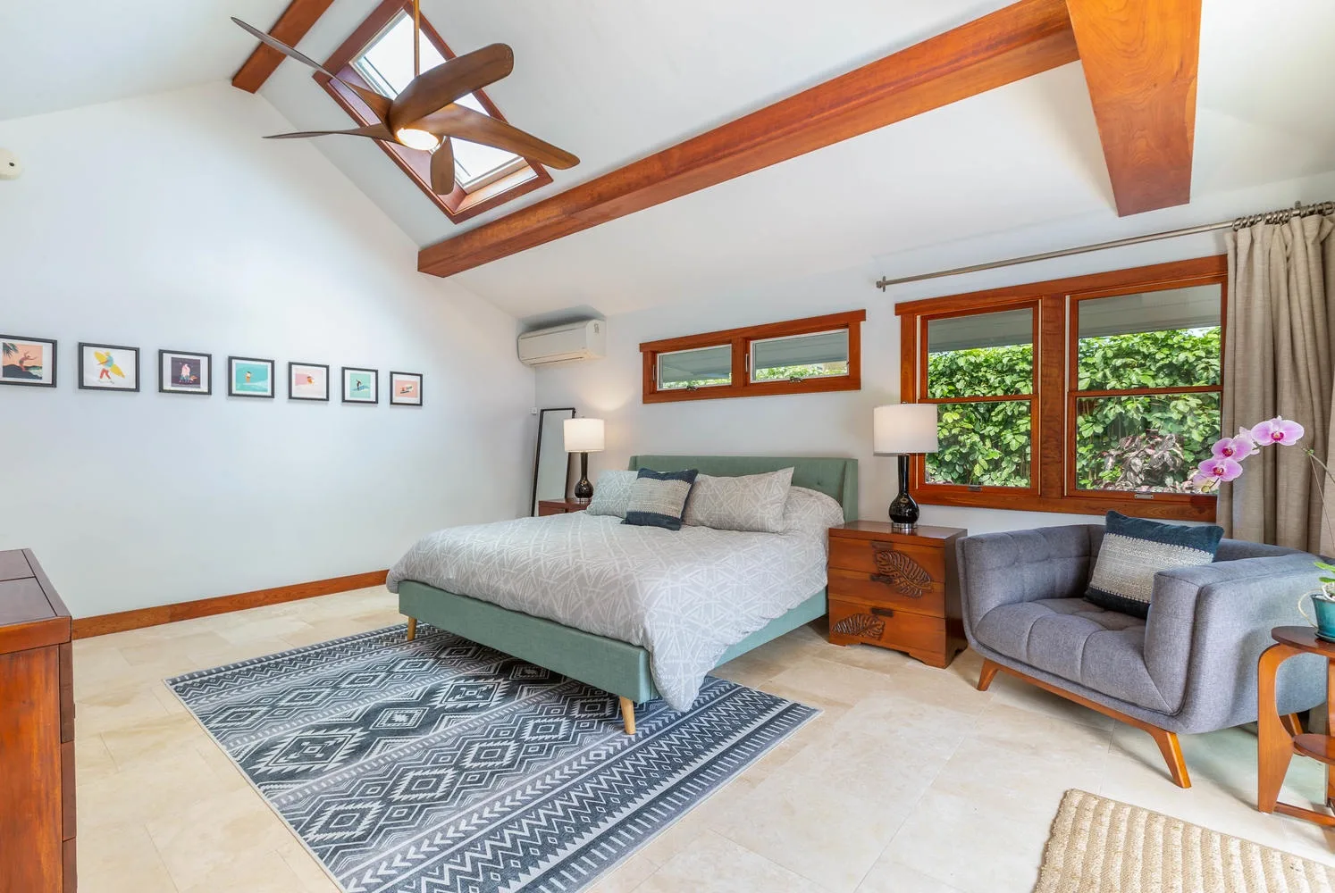A bright bedroom with a bed, a gray armchair, and large windows.