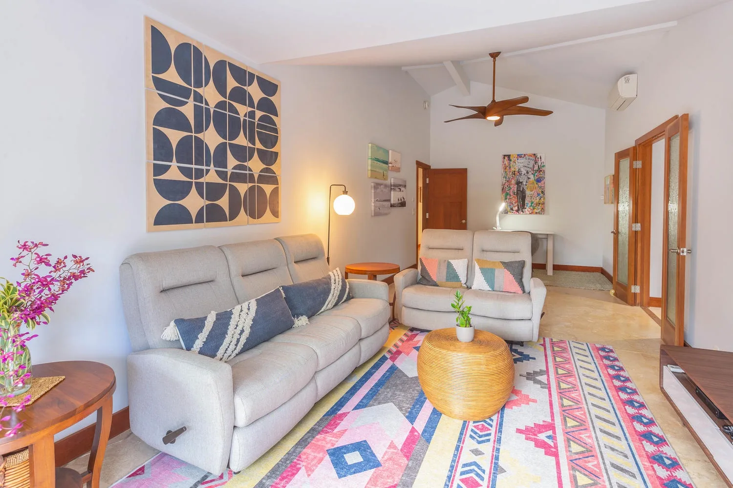 A bright living room with light seating, a colorful rug, and wall art.